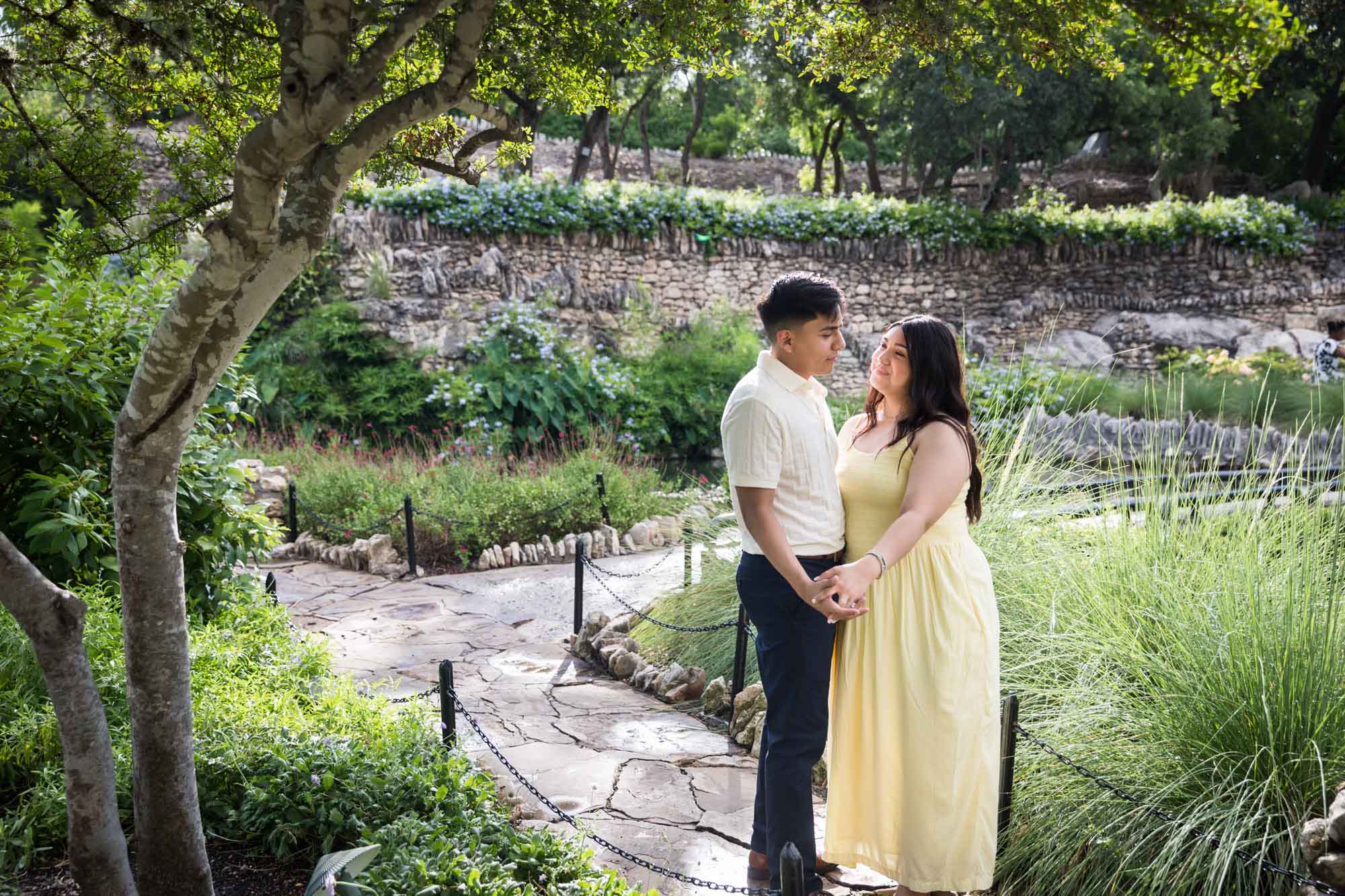 Man wearing white shirt hugging woman wearing yellow dress during a Japanese Tea Garden engagement portrait