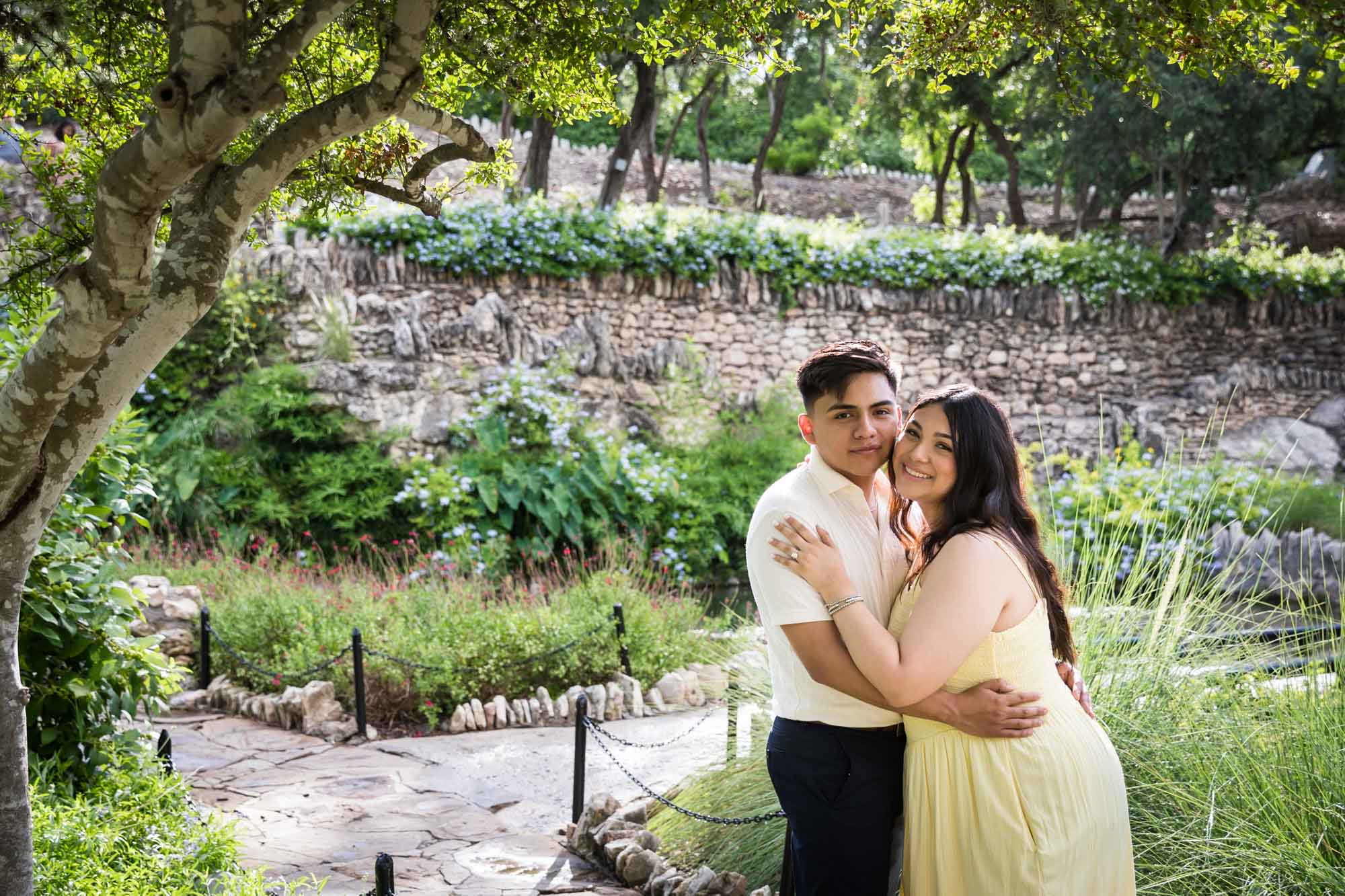Man wearing white shirt hugging woman wearing yellow dress during a Japanese Tea Garden engagement portrait
