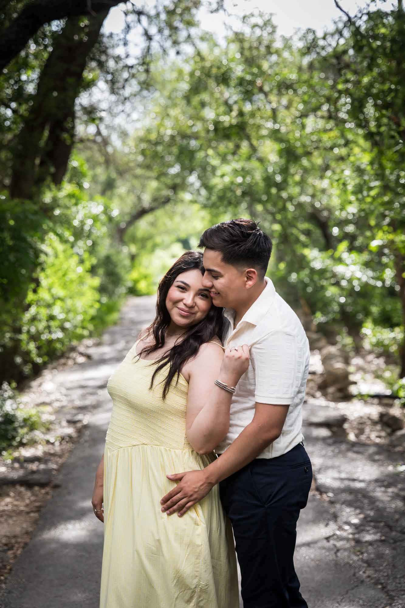 Man wearing white shirt hugging woman wearing yellow dress during a Japanese Tea Garden engagement portrait