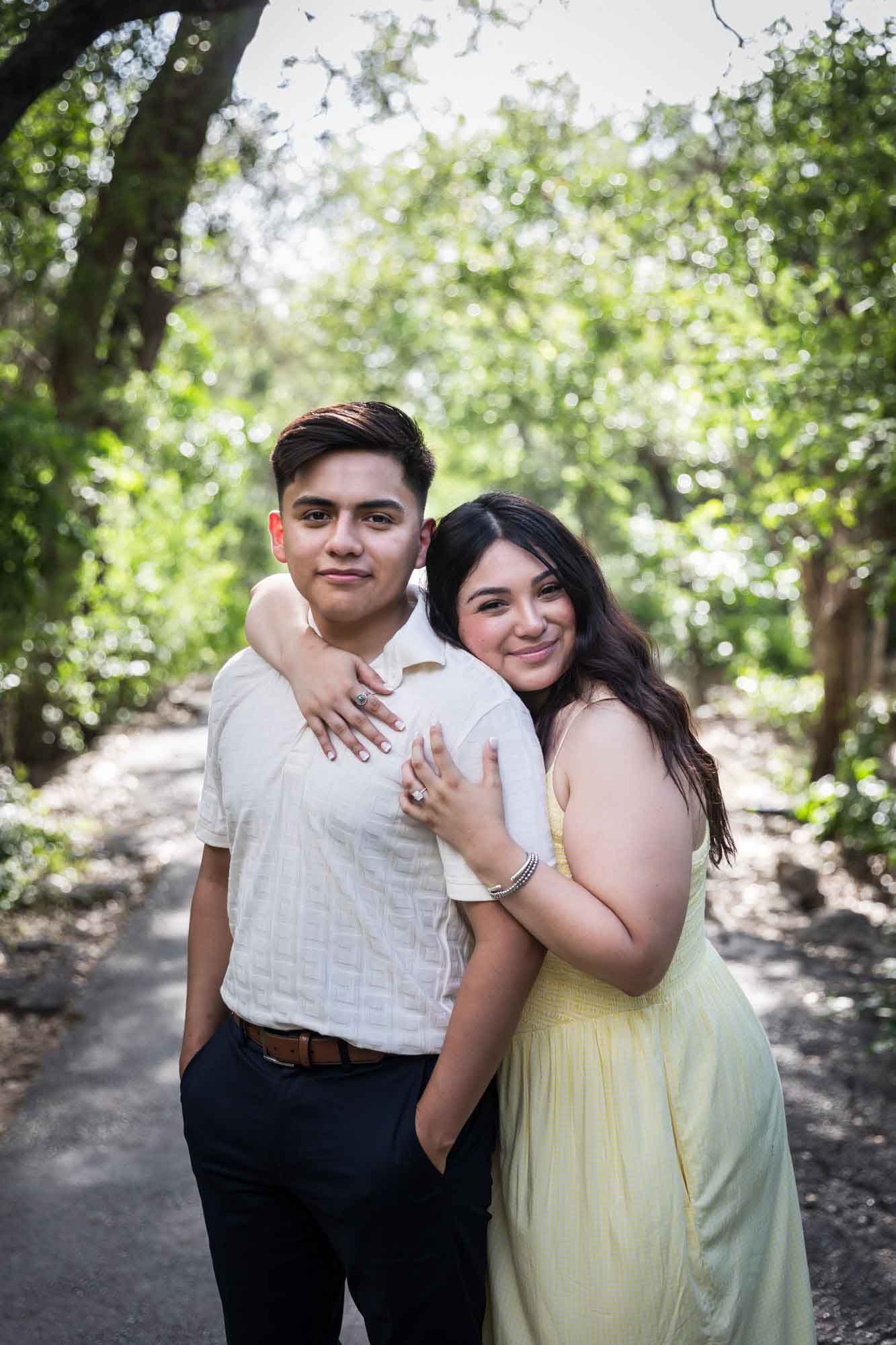 Man wearing white shirt hugging woman wearing yellow dress during a Japanese Tea Garden engagement portrait