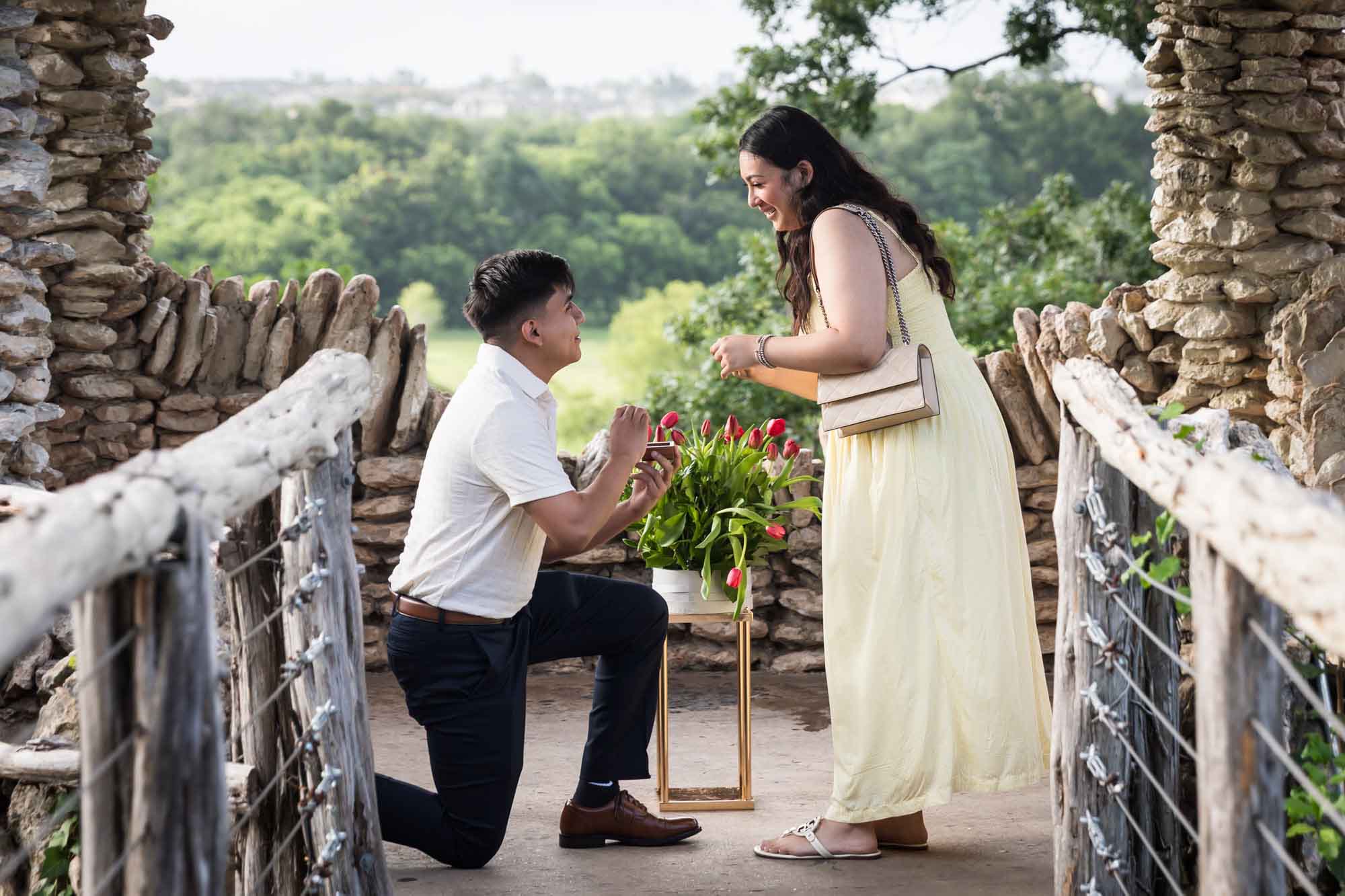 Man wearing black pants bending down on one knee in front of woman wearing yellow dress in stone gazebo during proposal for an article on Japanese Tea Garden proposal tips