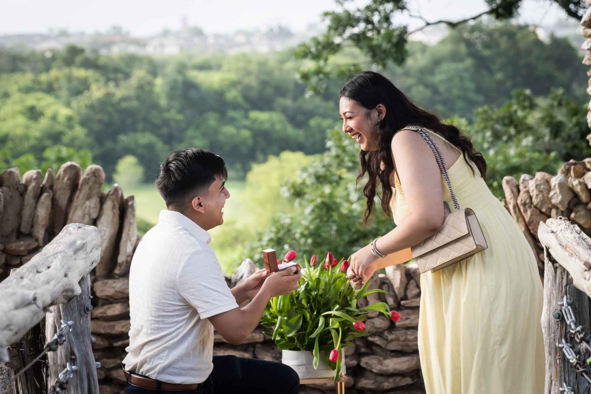 Man wearing black pants bending down on one knee in front of woman wearing yellow dress in stone gazebo during proposal for an article on Japanese Tea Garden proposal tips