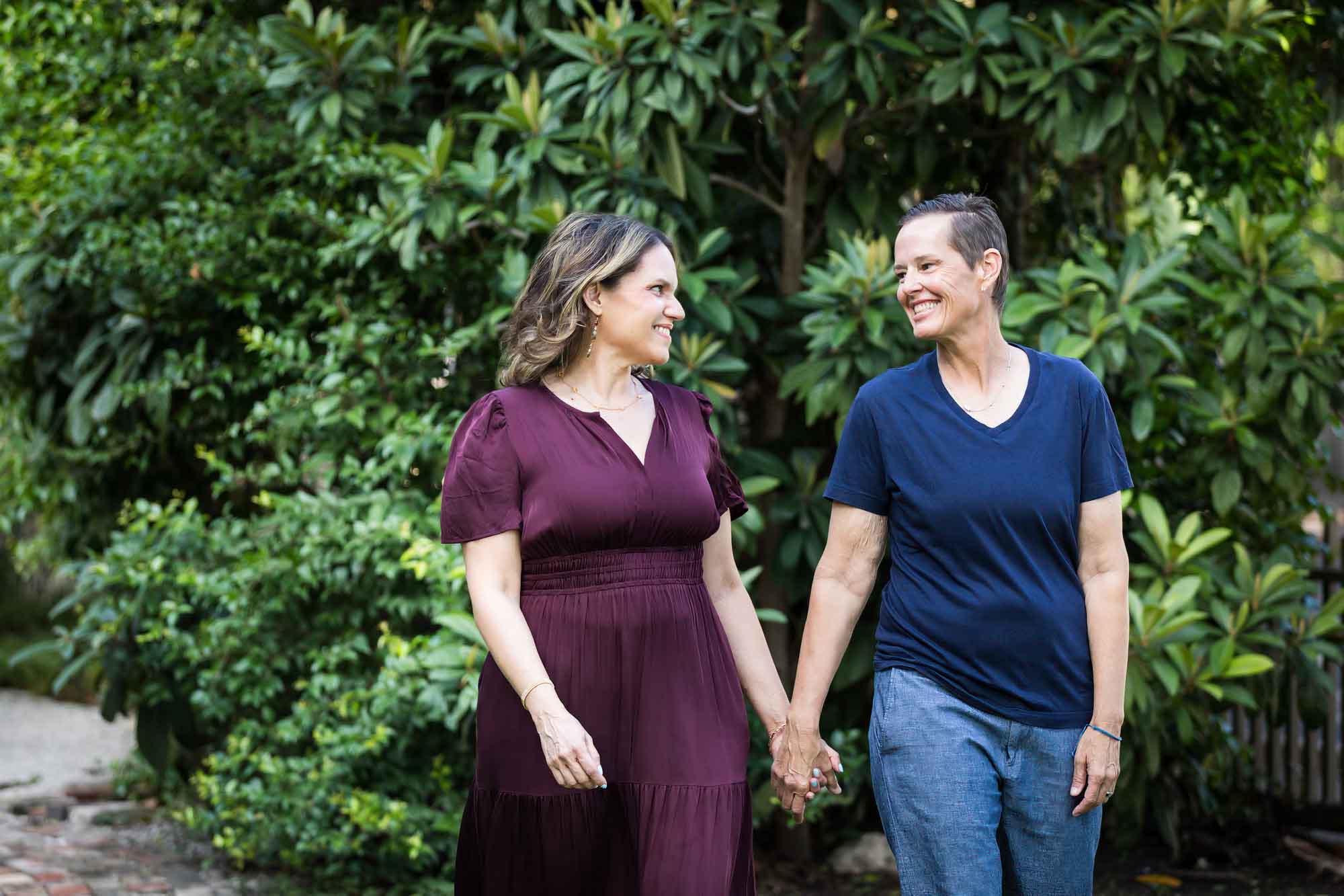 Two women holding hands walking in front of trees during a King William family portrait