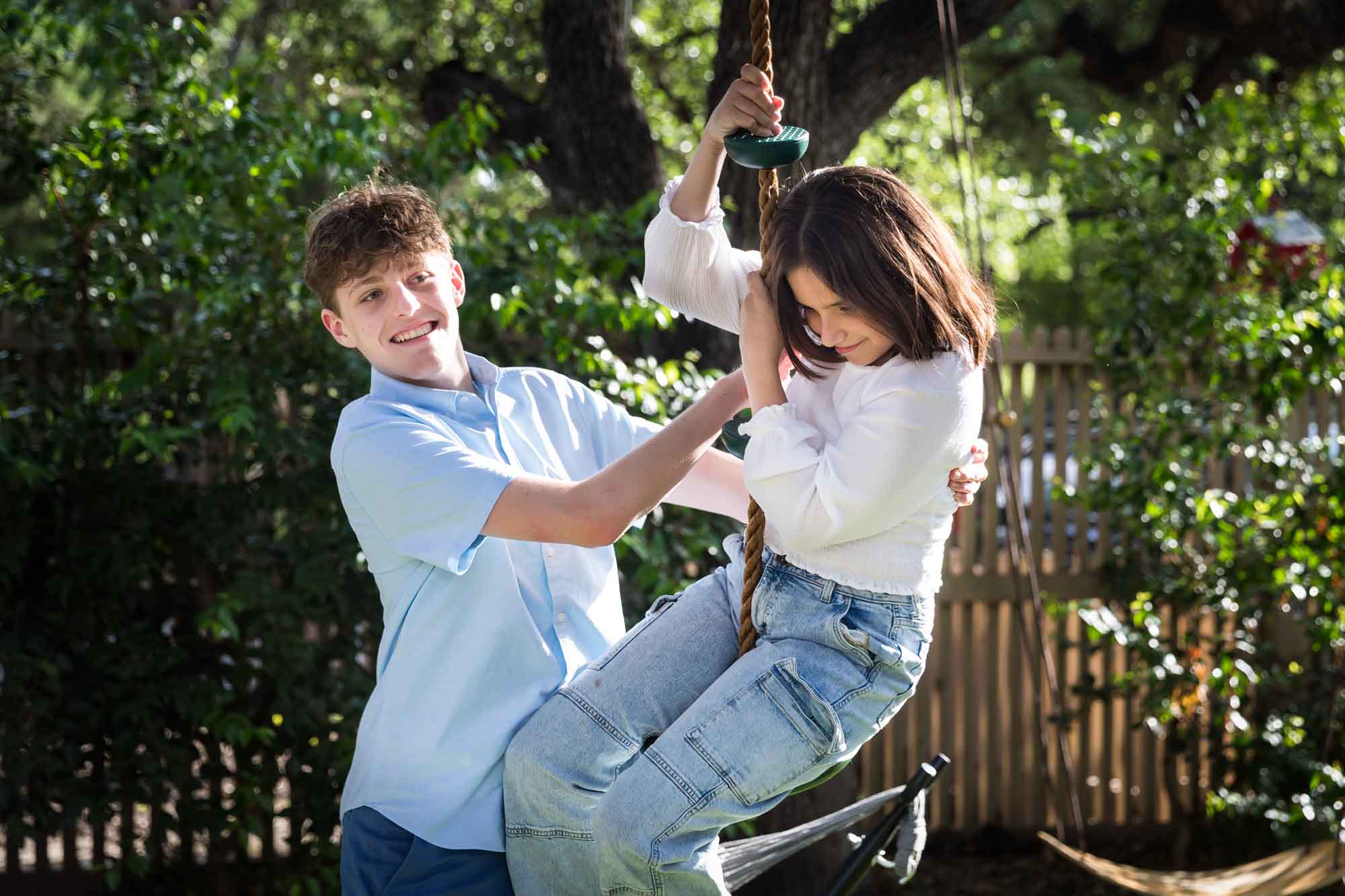 Teenage boy and girl playing on swing in backyard during a King William family portrait