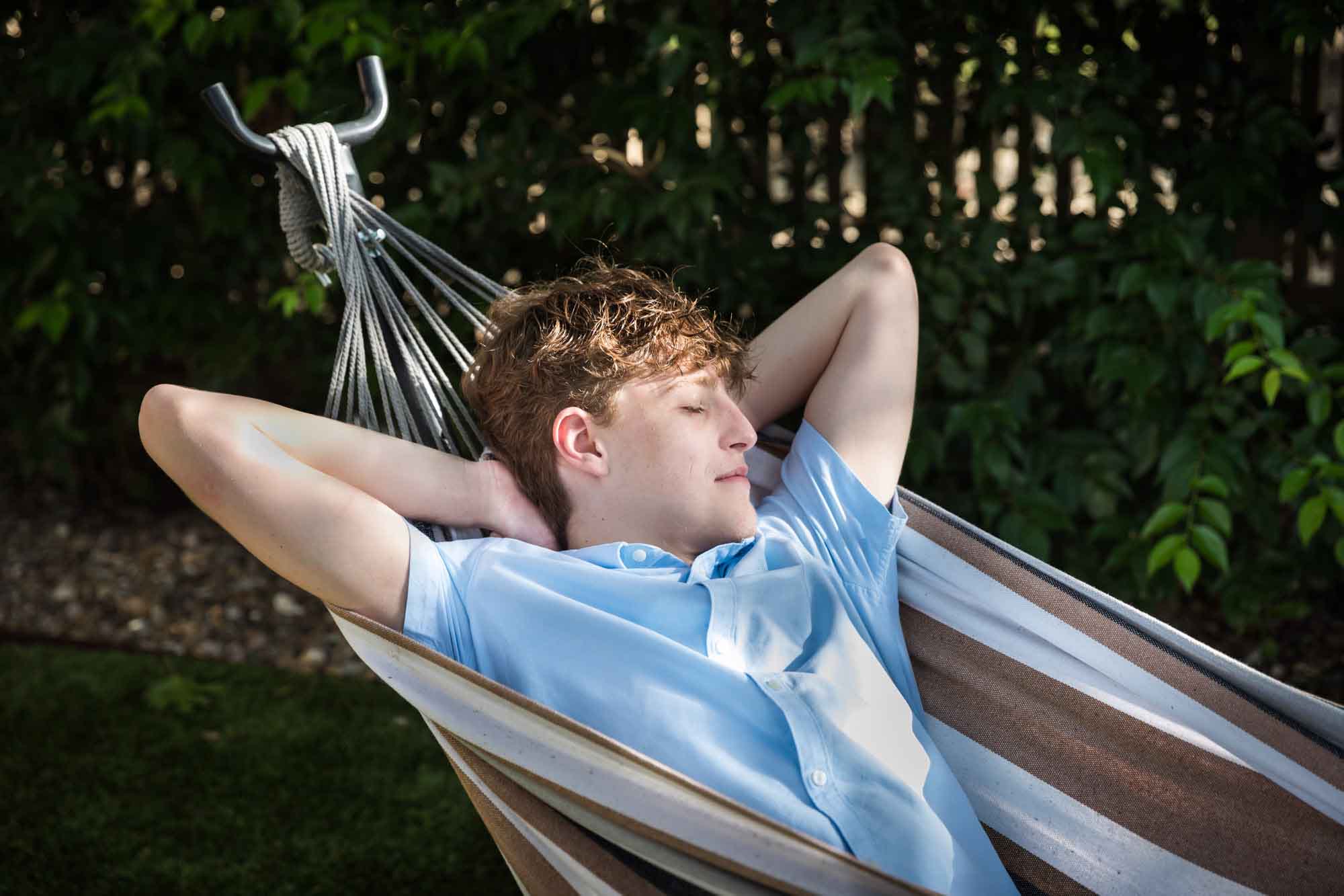Teenage boy relaxing with eyes closed in hammock with arms behind his head during a King William family portrait