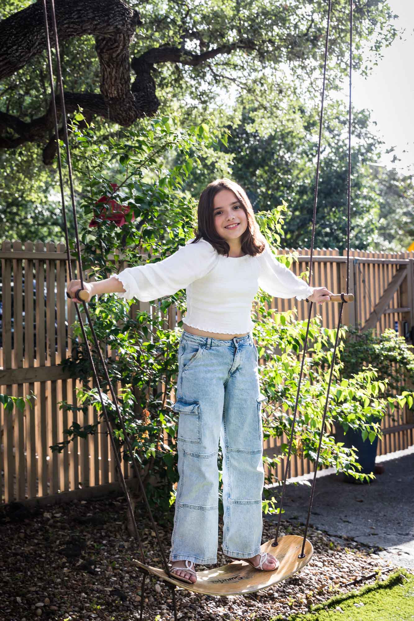 Teenage girl wearing white blouse and jeans standing on swing during a King William family portrait
