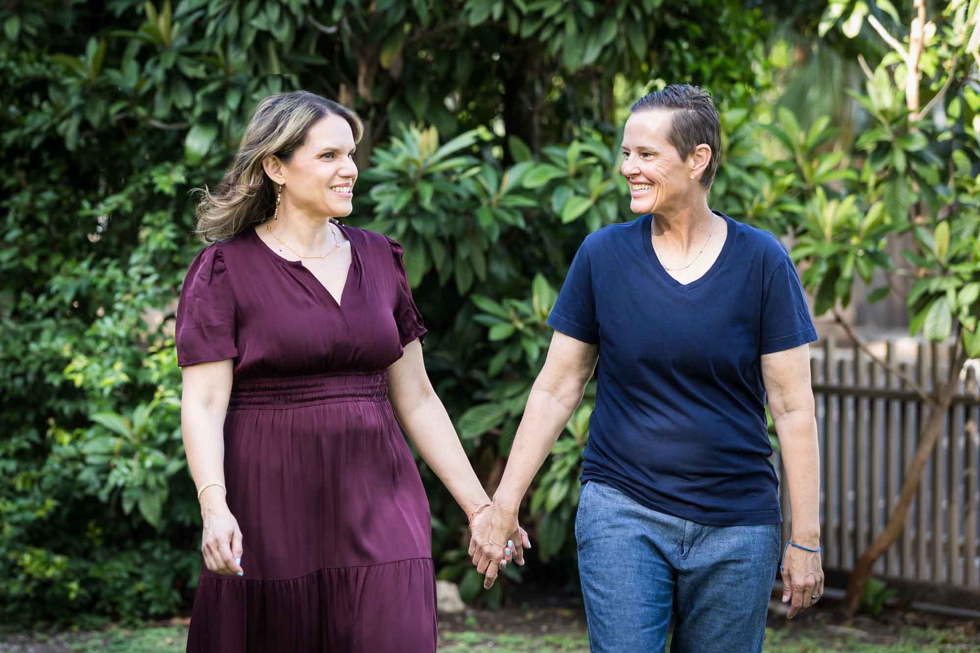Two women holding hands walking in front of trees during a King William family portrait