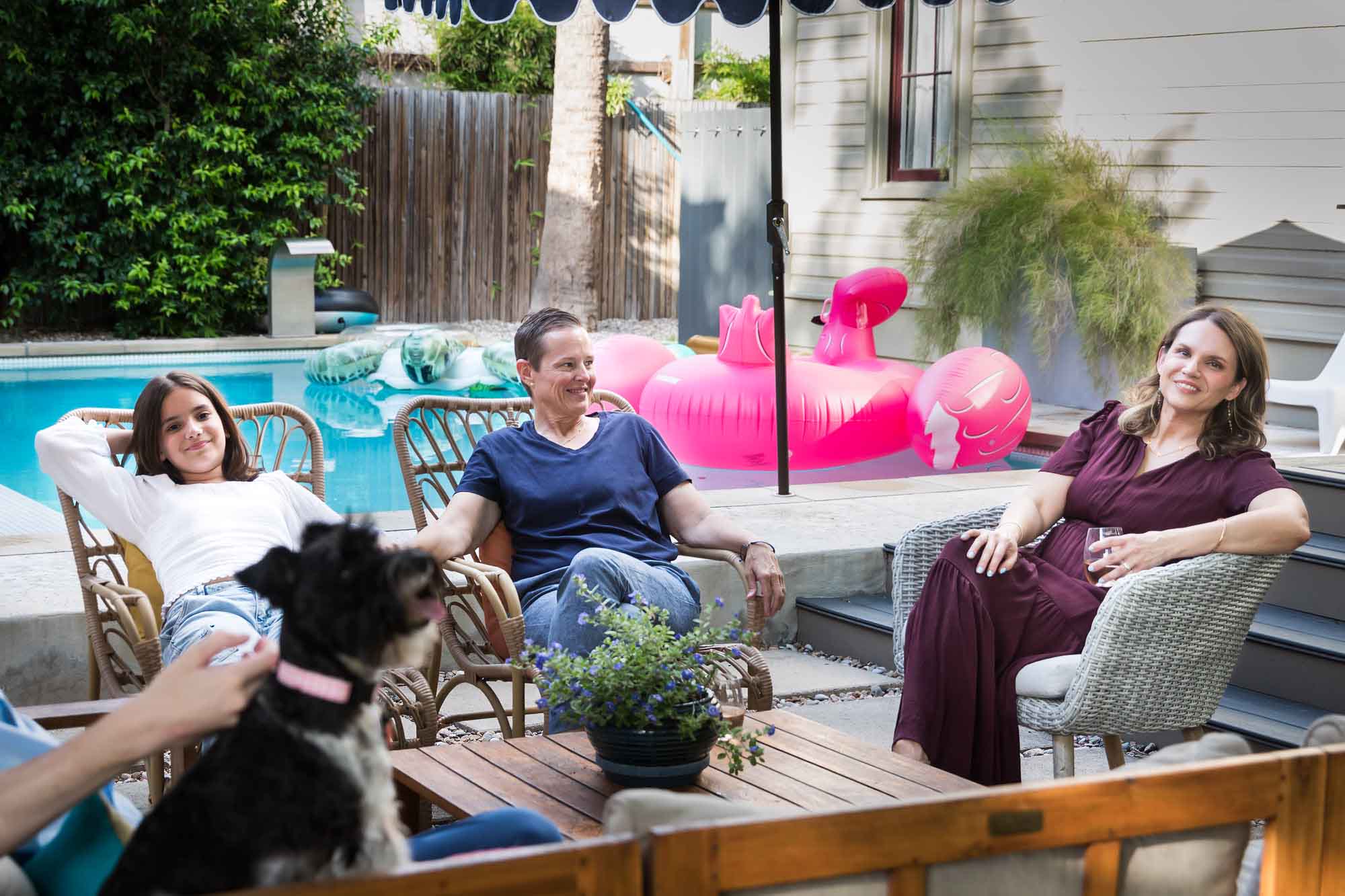 Family of two mothers and teenage girl seated around table near pool relaxing during a King William family portrait