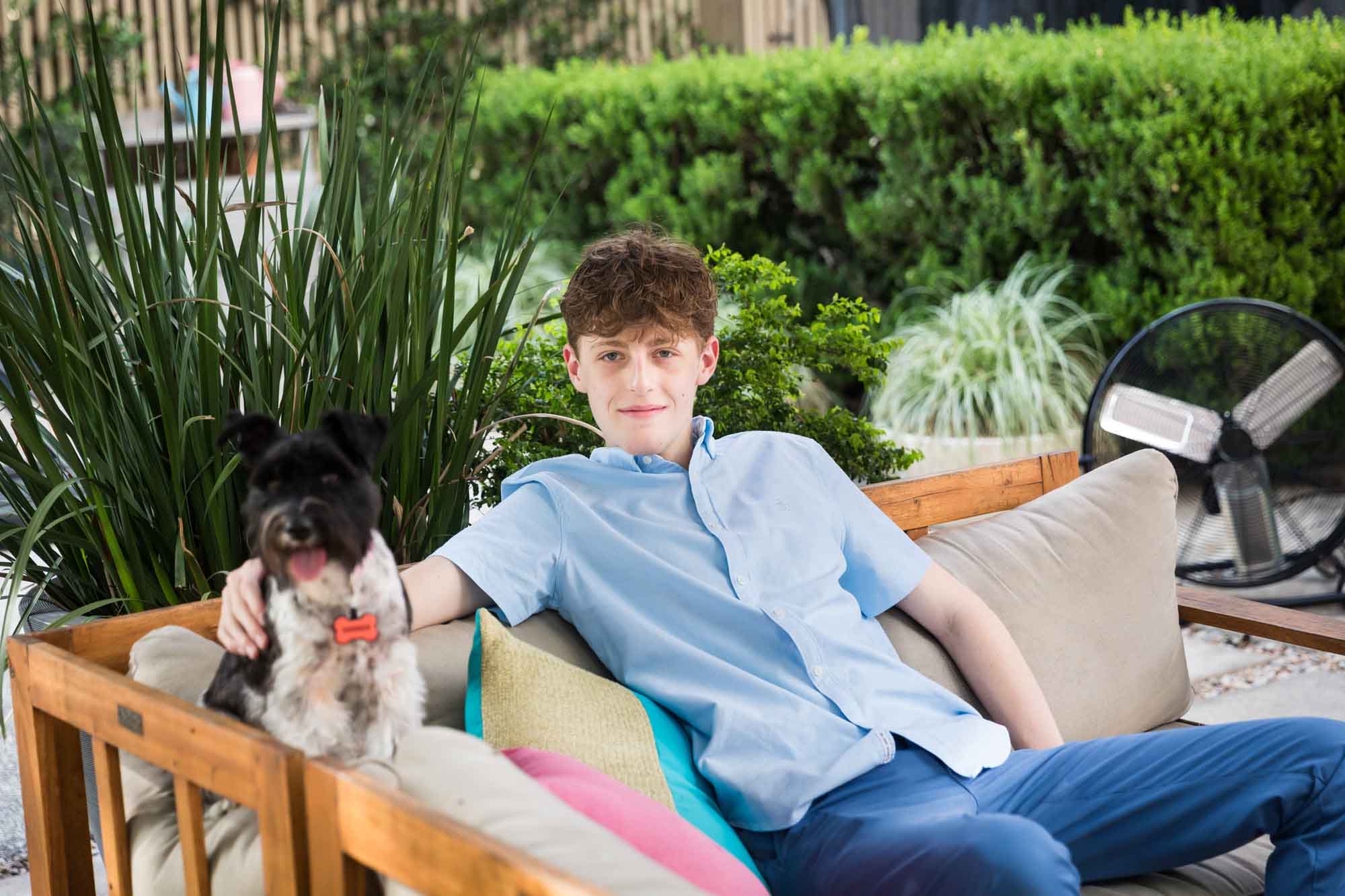 Teenage boy wearing blue shirt and pants seated on sofa with dog during a King William family portrait