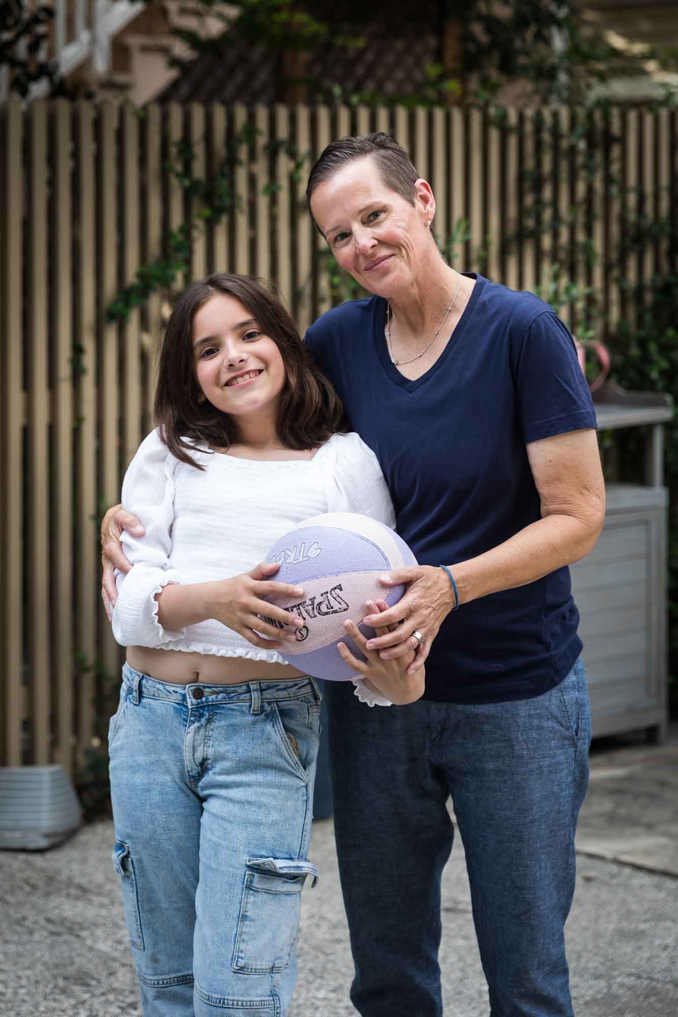 Mother and teenage daughter holding basketball in front of fence during a King William family portrait