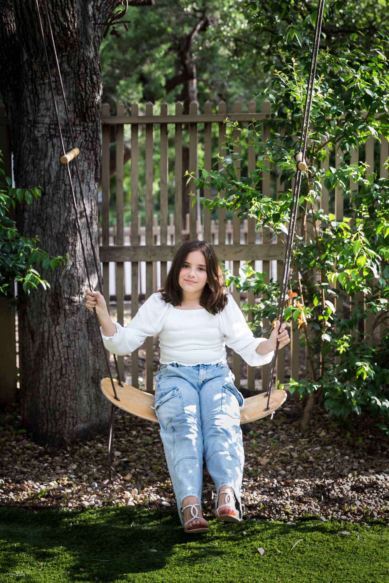 Teenage girl wearing white blouse and jeans standing on swing during a King William family portrait