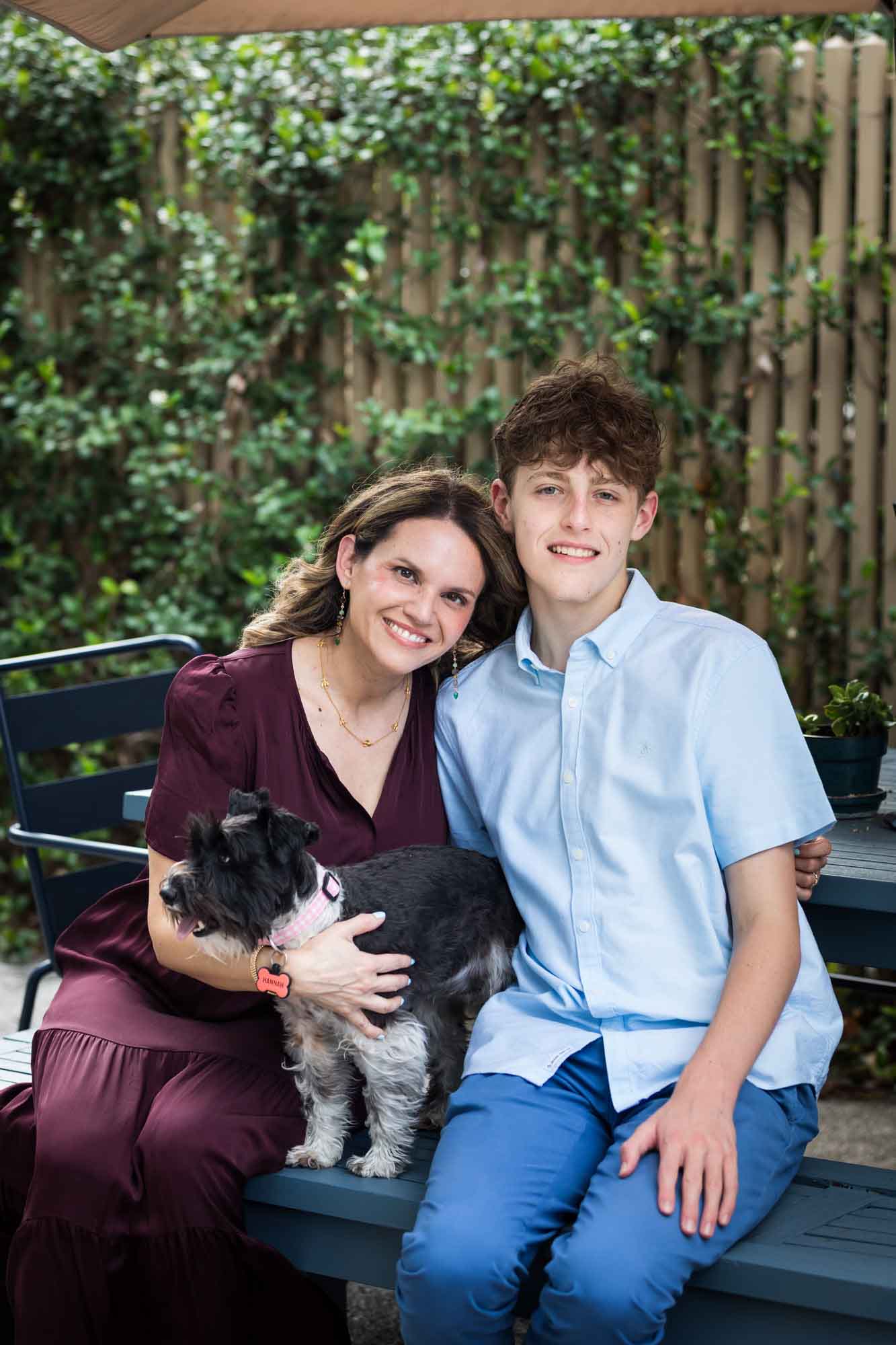 Mother wearing maroon dress seated with son wearing blue shirt and dog Teenage girl wearing white blouse and jeans standing on swing during a King William family portrait