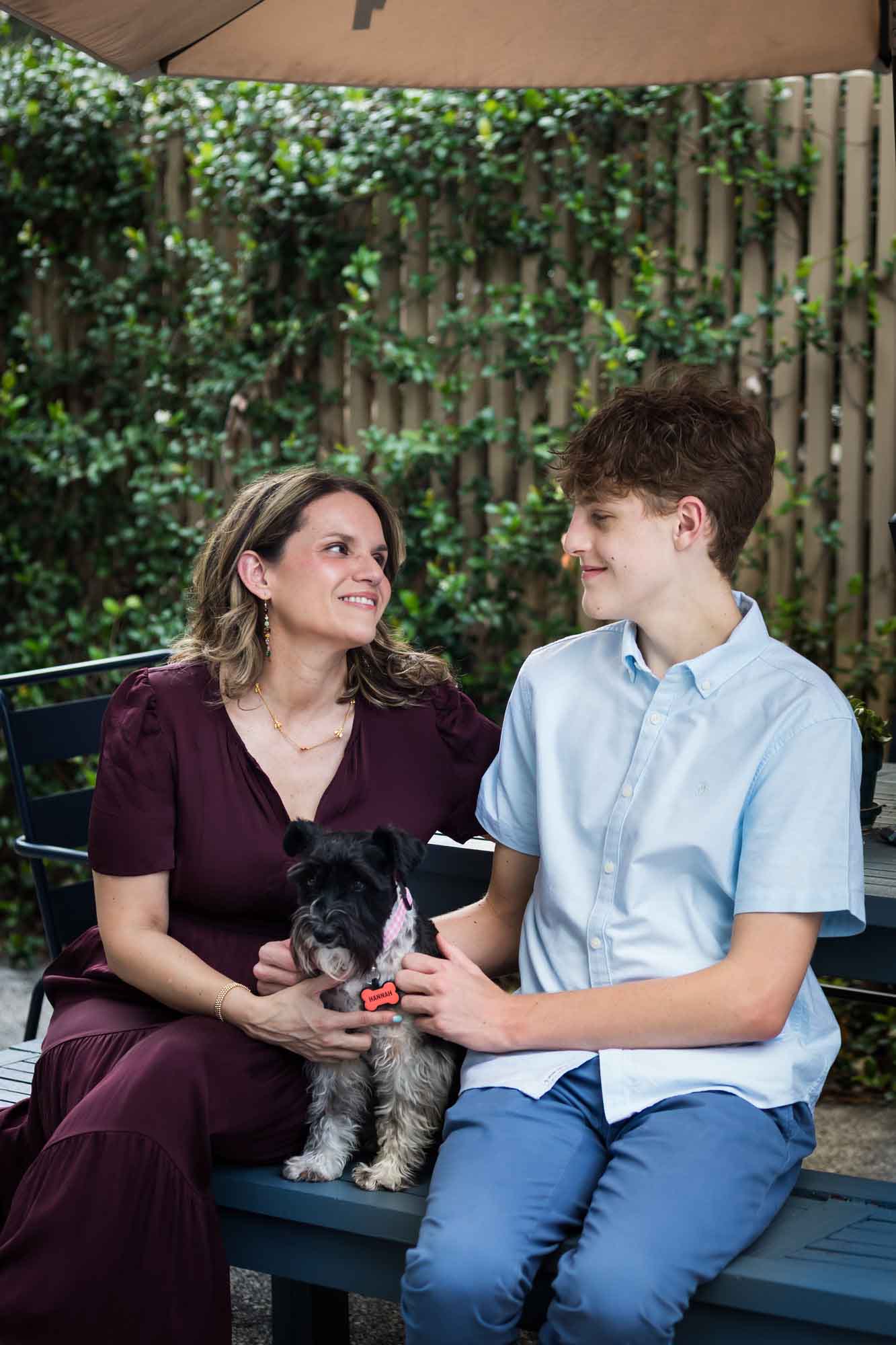 Mother wearing maroon dress seated with son wearing blue shirt and dog Teenage girl wearing white blouse and jeans standing on swing during a King William family portrait