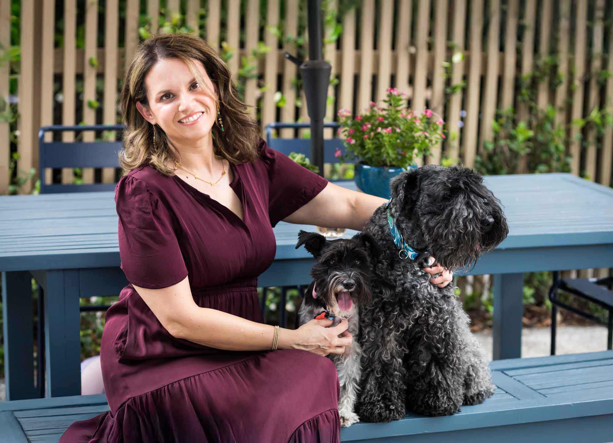 Mother wearing maroon dress seated on blue picnic bench with two dogs Mother wearing navy t-shirt hugging daughter wearing white shirt playing on swing Mother wearing maroon dress seated with son wearing blue shirt and dog Teenage girl wearing white blouse and jeans standing on swing during a King William family portrait