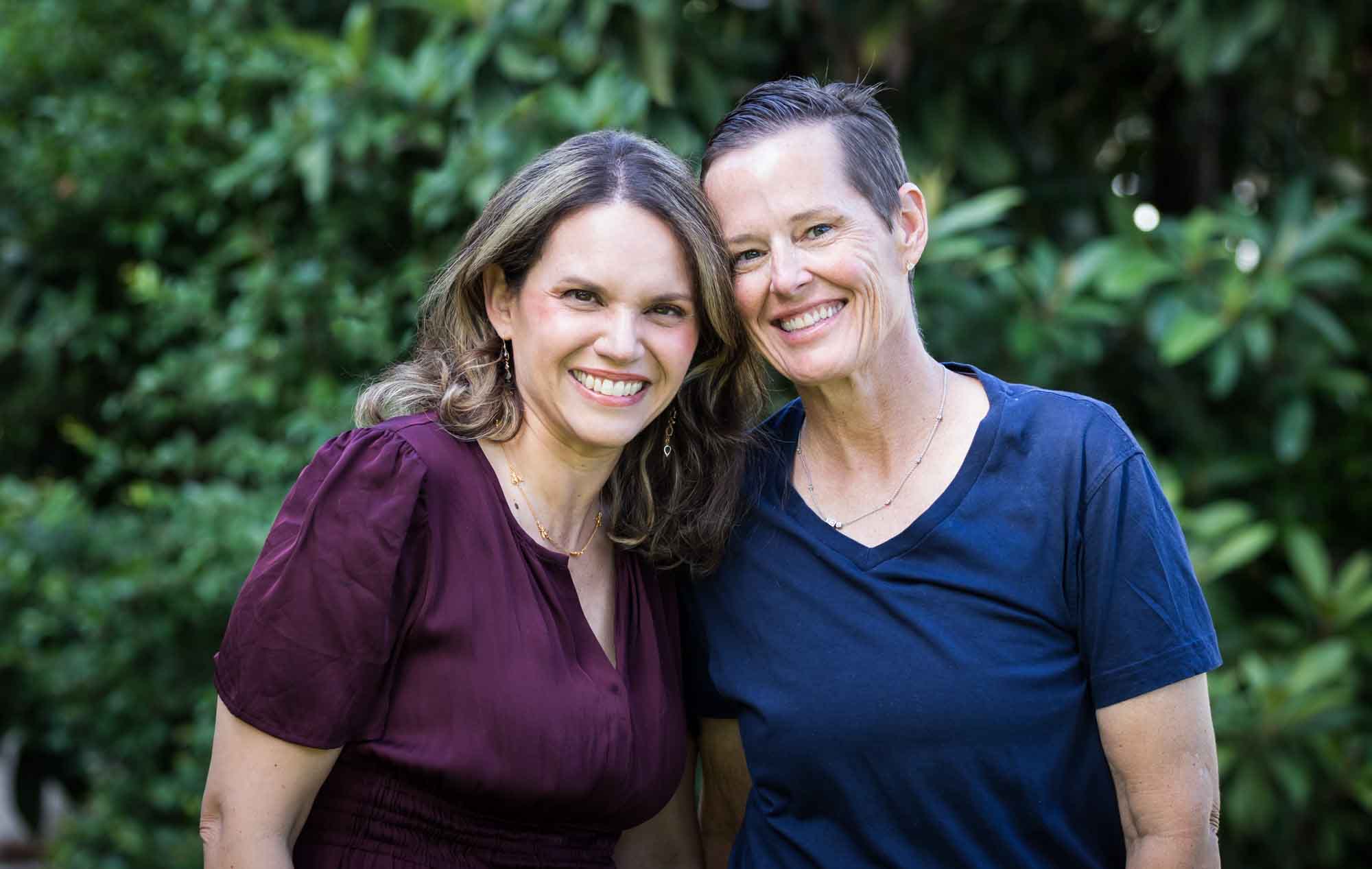 Two women hugging and touching foreheads in front of trees during a King William family portrait