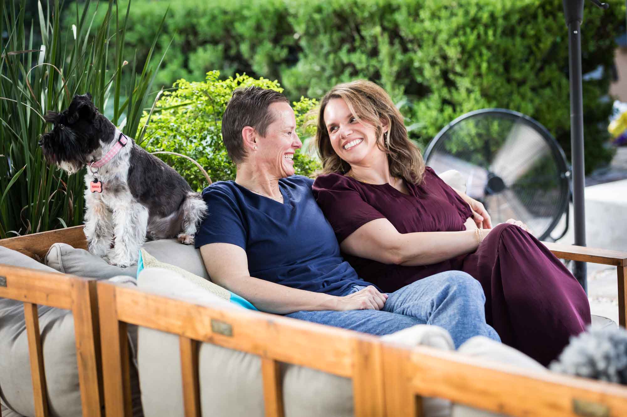 Two women seated on sofa with dog with umbrella in background Mother wearing navy t-shirt seated in hammock with teenage son wearing blue shirt during a King William family portrait