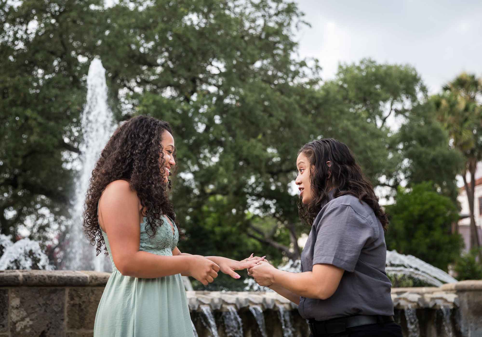 Woman putting engagement ring on another woman's hand in front of fountain for an article about McNay Art Museum proposal tips