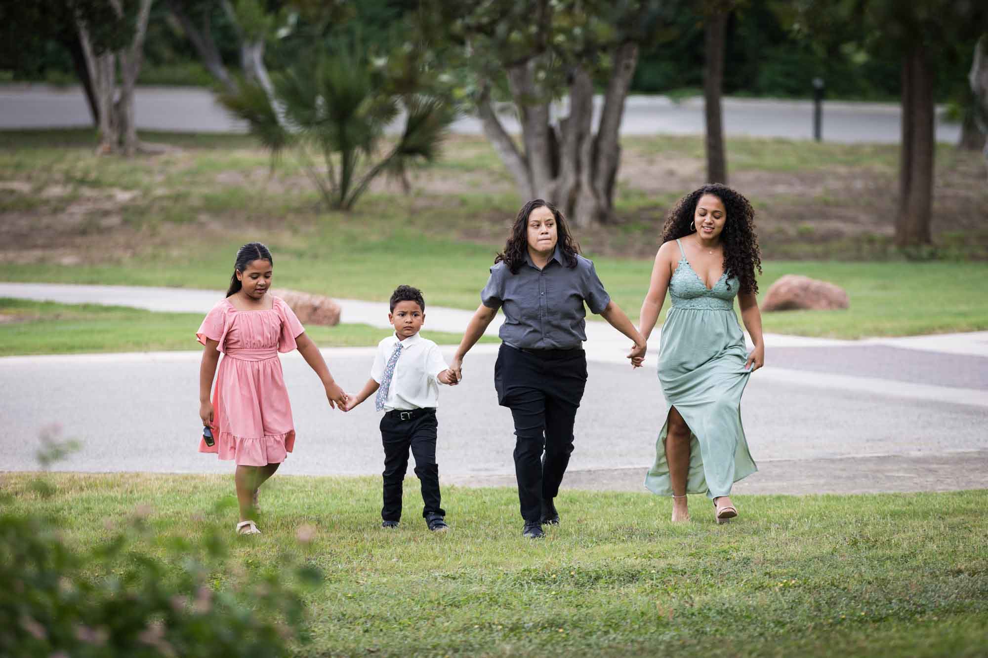 Two women holding hands with little boy and little girl walking in the grass