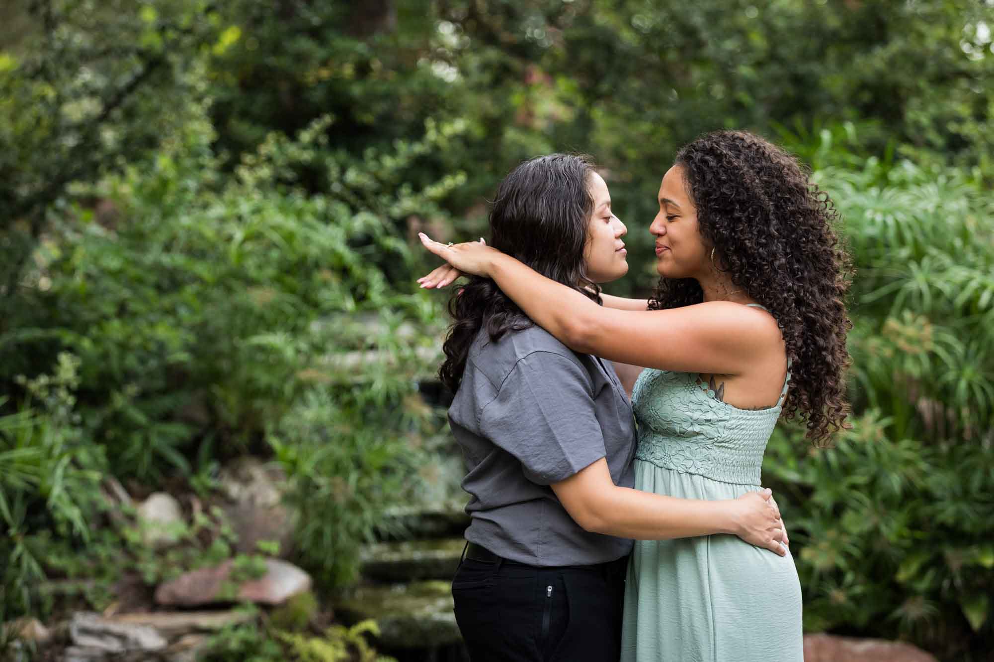 Two women hugging with green bushes and trees in background for an article about McNay Art Museum proposal tips