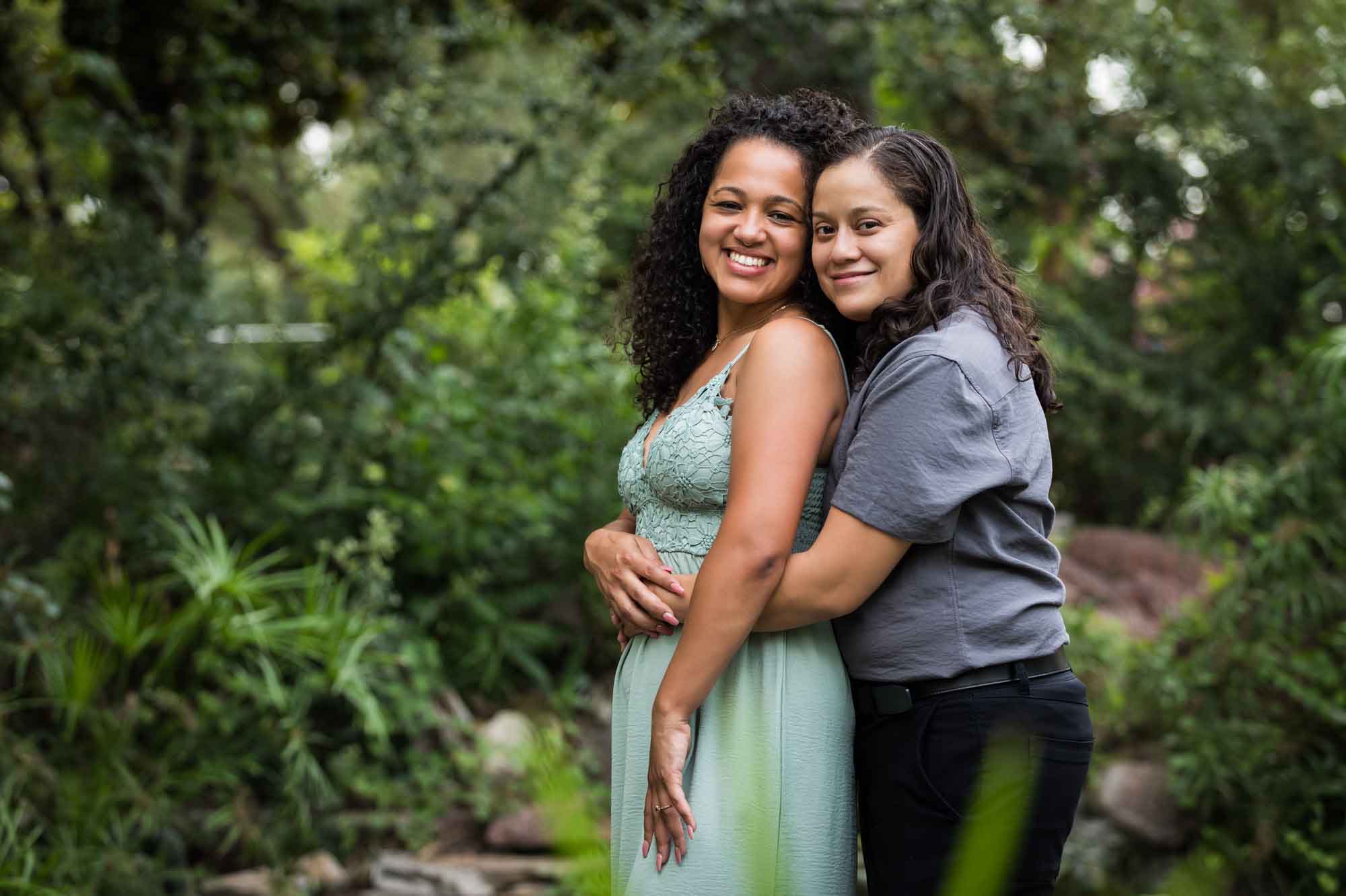 Two women hugging with green bushes and trees in background for an article about McNay Art Museum proposal tips