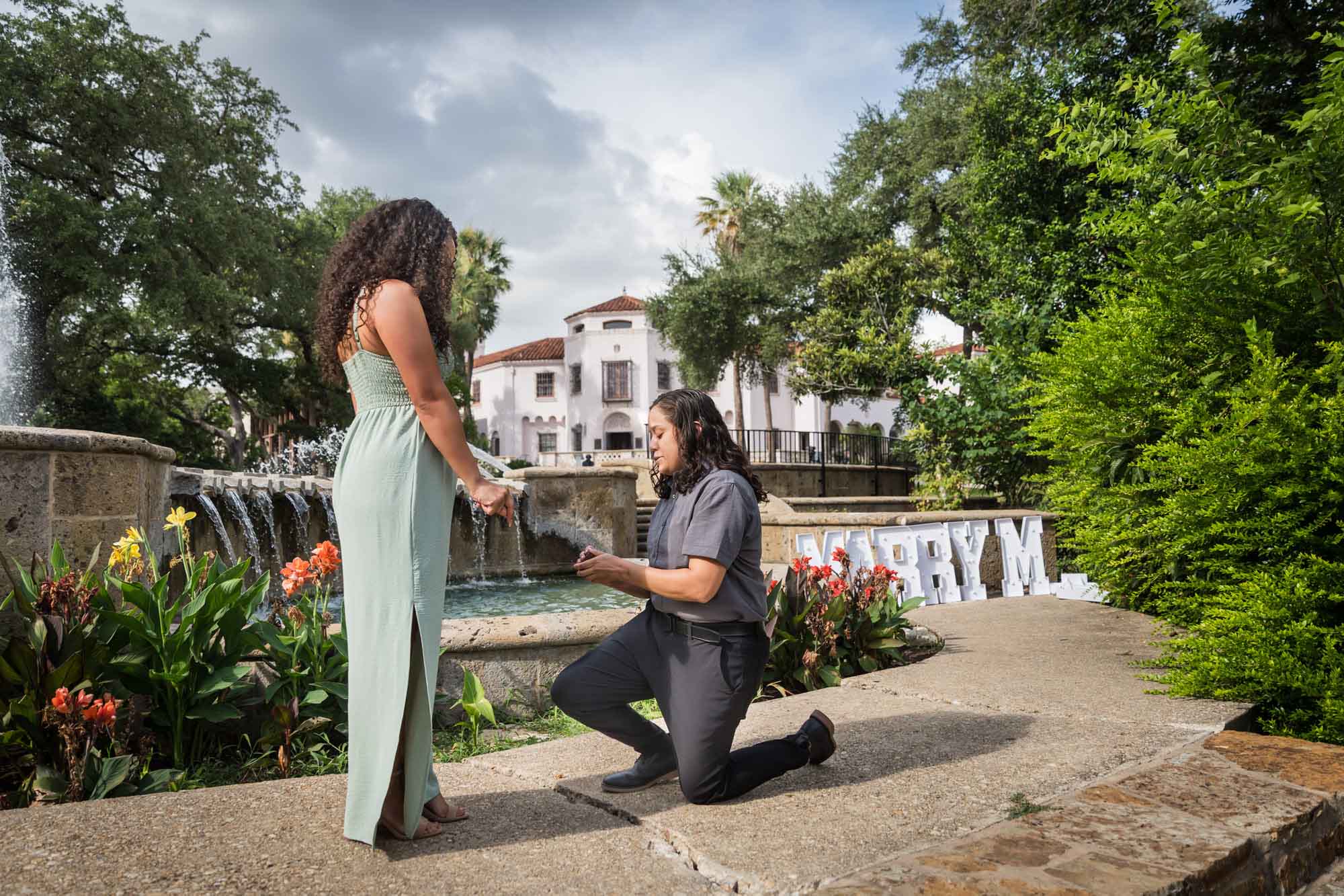 Woman proposing to another woman in front of fountain for an article about McNay Art Museum proposal tips