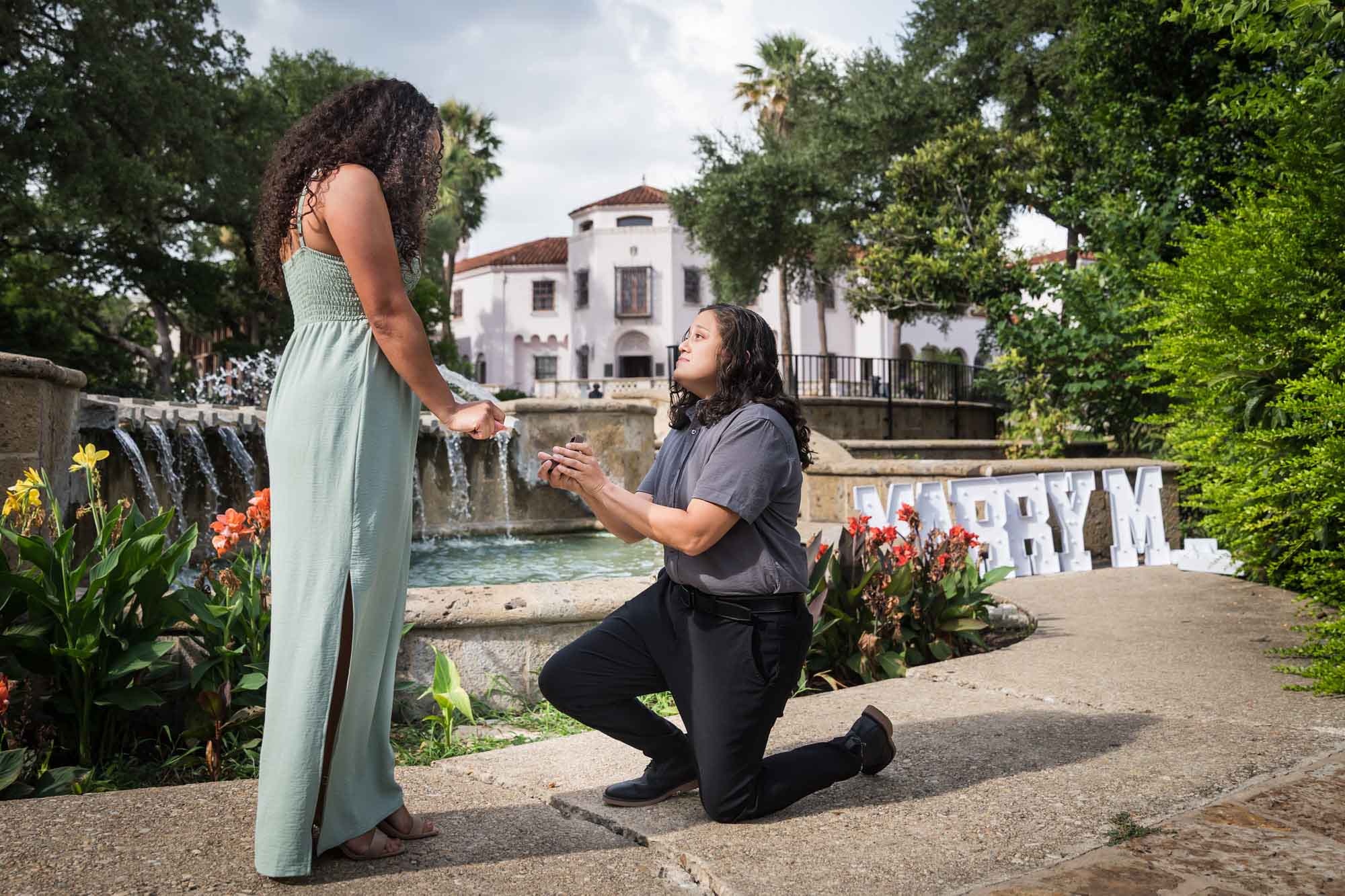 Woman proposing to another woman in front of fountain for an article about McNay Art Museum proposal tips