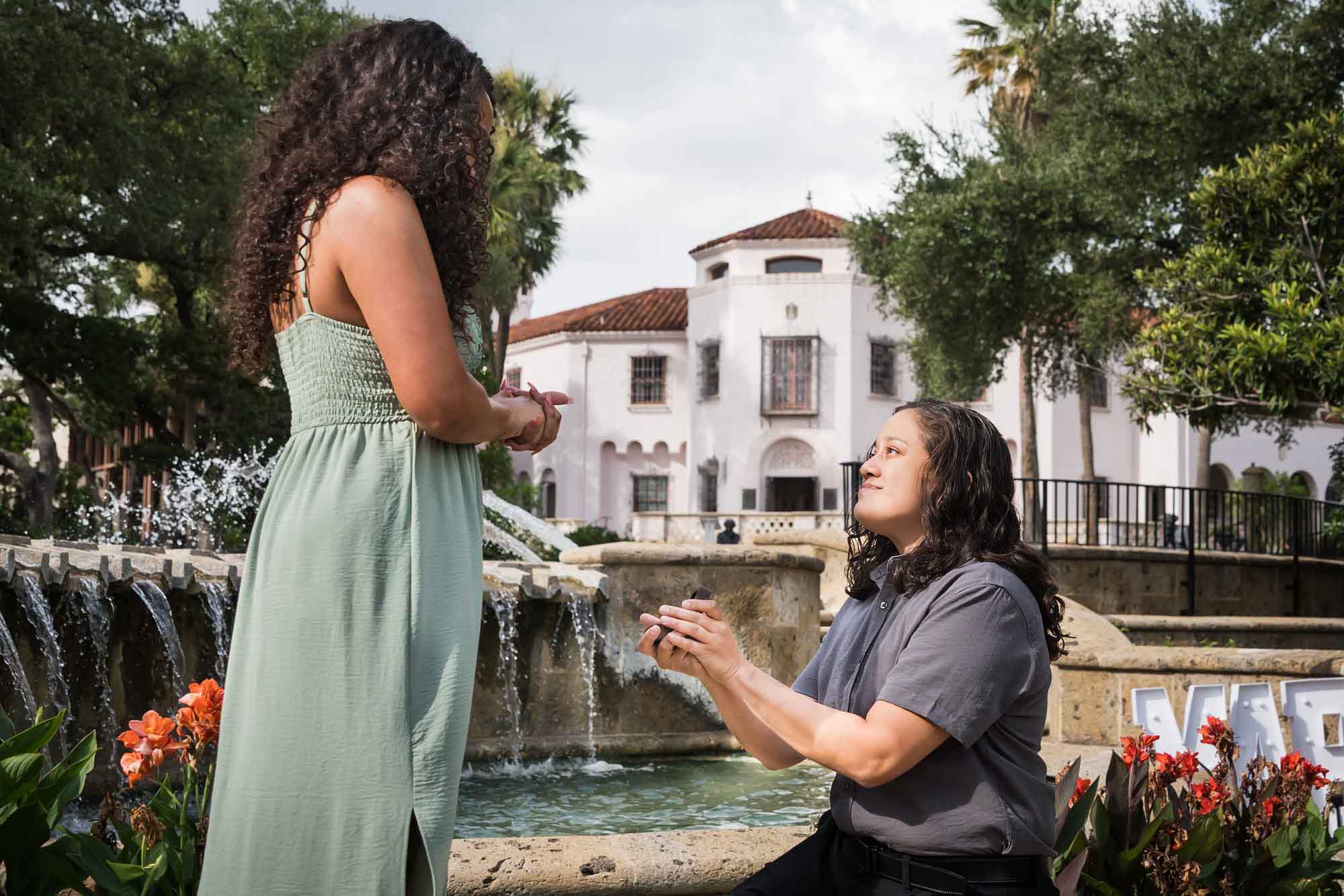 Woman proposing to another woman in front of fountain for an article about McNay Art Museum proposal tips