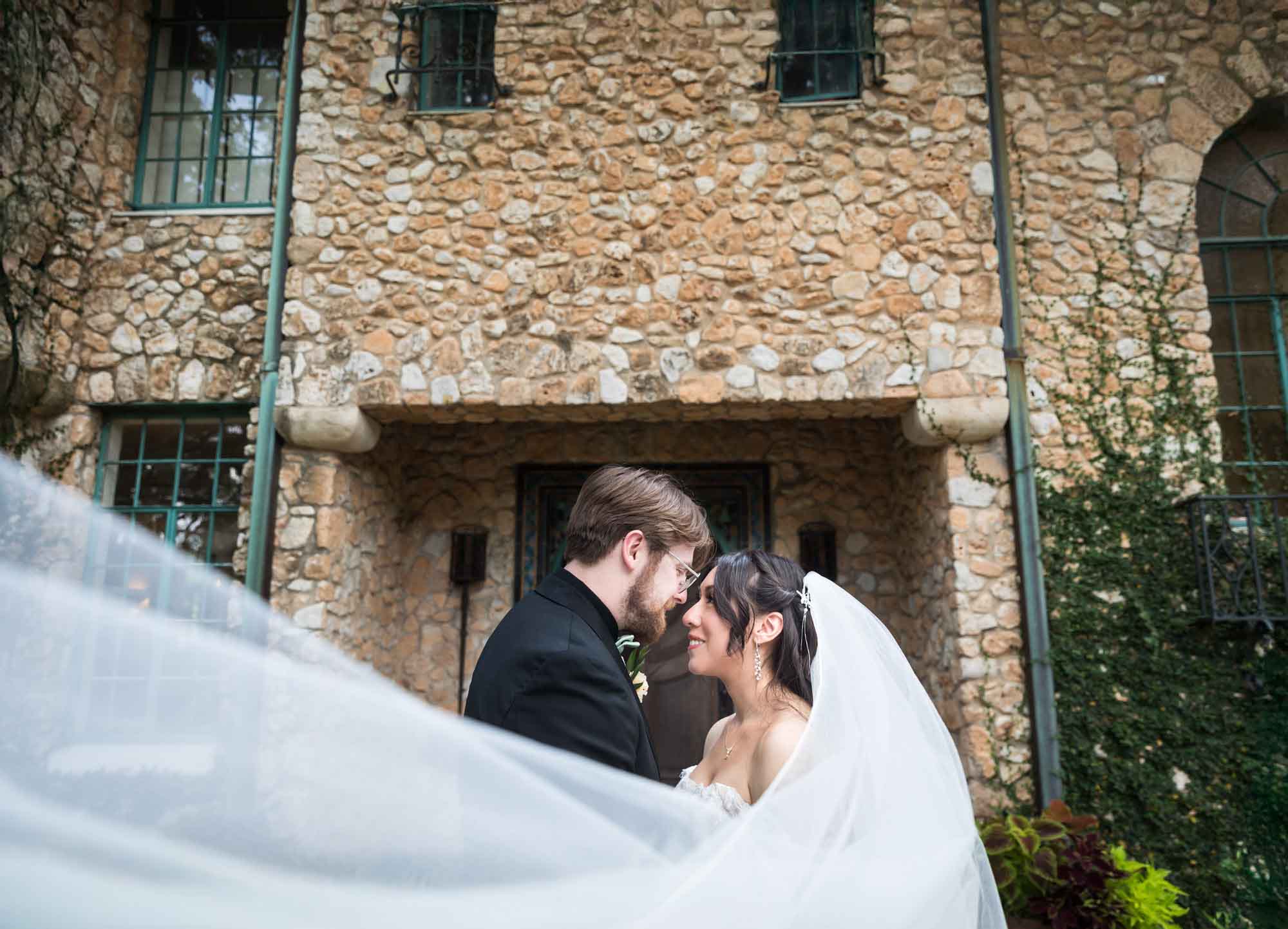 Bride and groom looking at each other seated in front of stone entrance of The Veranda for an article on affordable wedding venues in San Antonio
