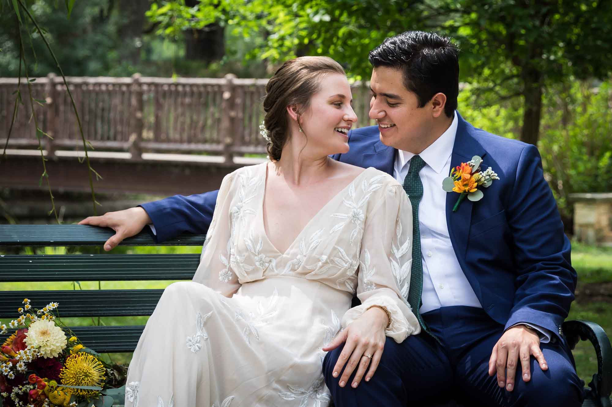 Bride and groom sitting on bench looking at each other in Landa Park for an article on affordable wedding venues in San Antonio