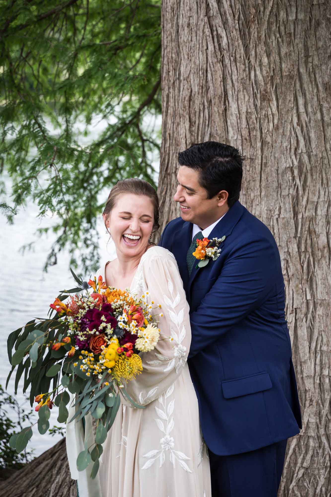 Bride holding large colorful flower bouquet and groom hugging in front of large tree for an article on affordable wedding venues in San Antonio