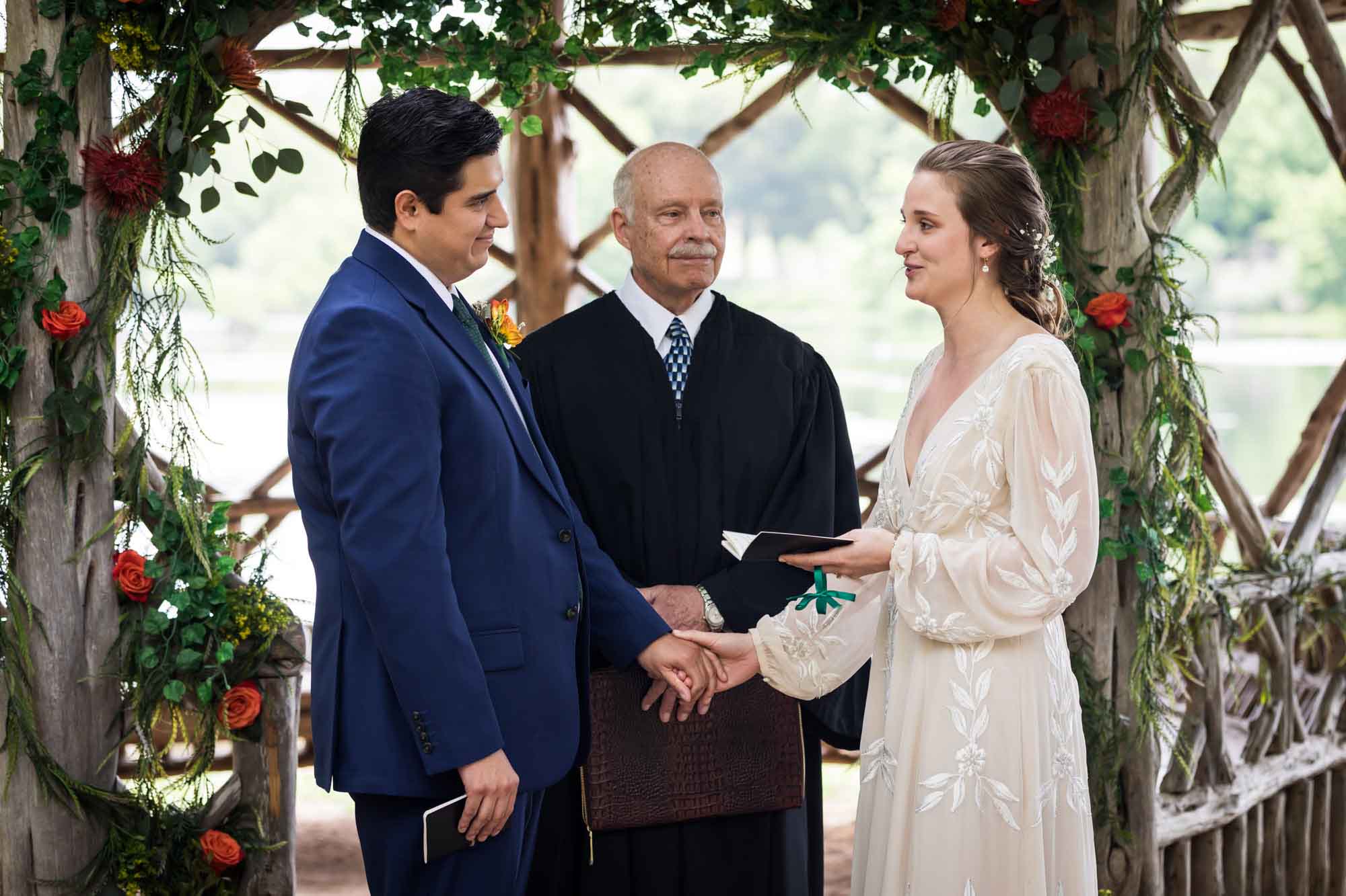 Bride and groom holding hands and saying vows in front of officiant wearing black robe at Landa Park gazebo for an article on affordable wedding venues in San Antonio