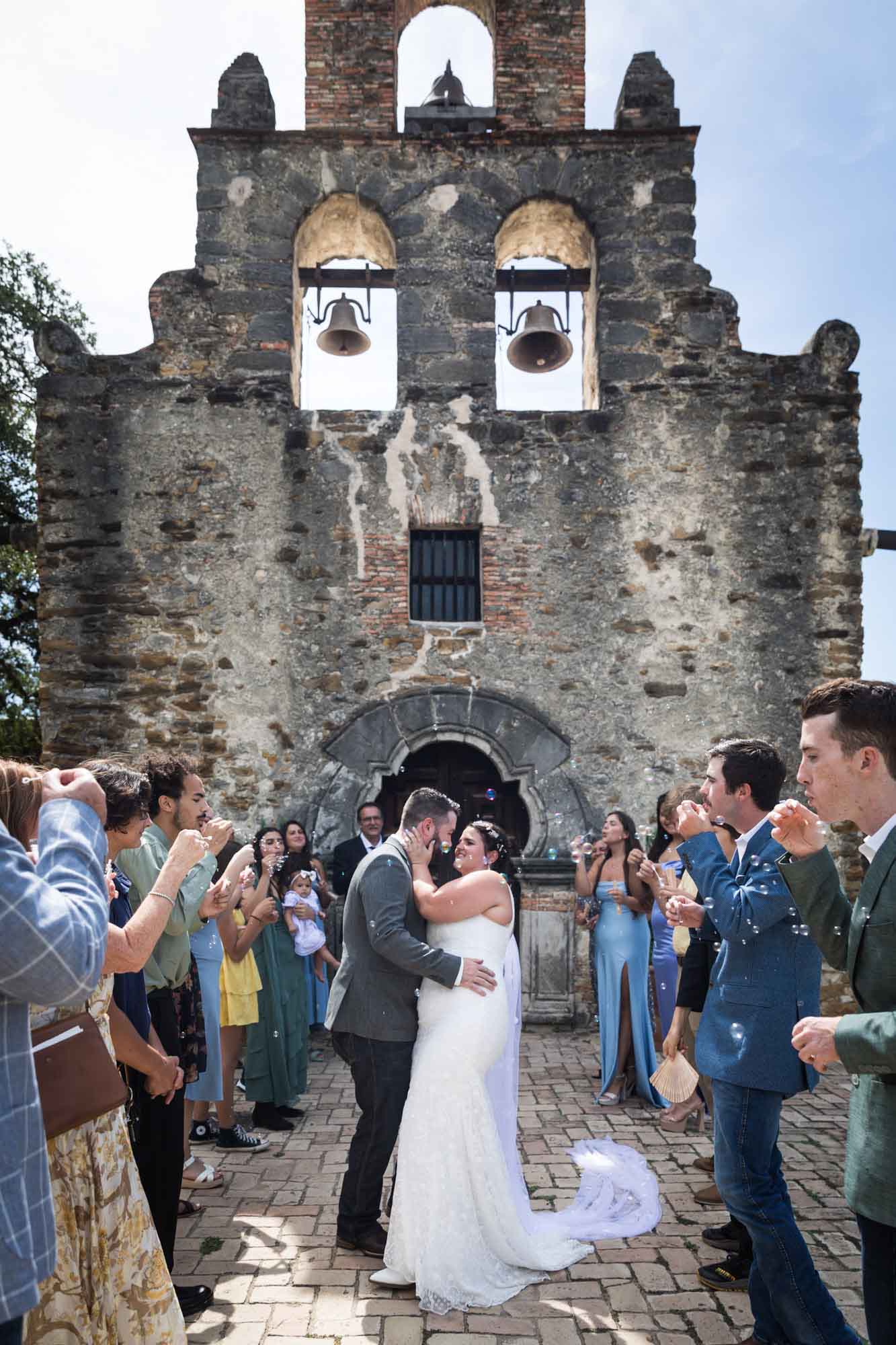 Bride and groom about to kiss in front of guests in front of Mission Espada for an article on affordable wedding venues in San Antonio