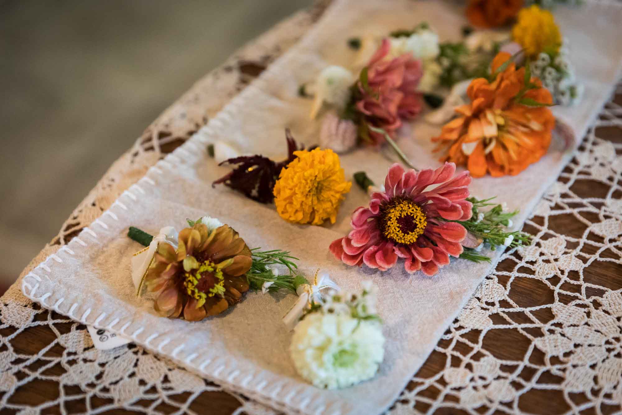 Homemade corsages made of colorful flowers resting on table with lace tablecloth
