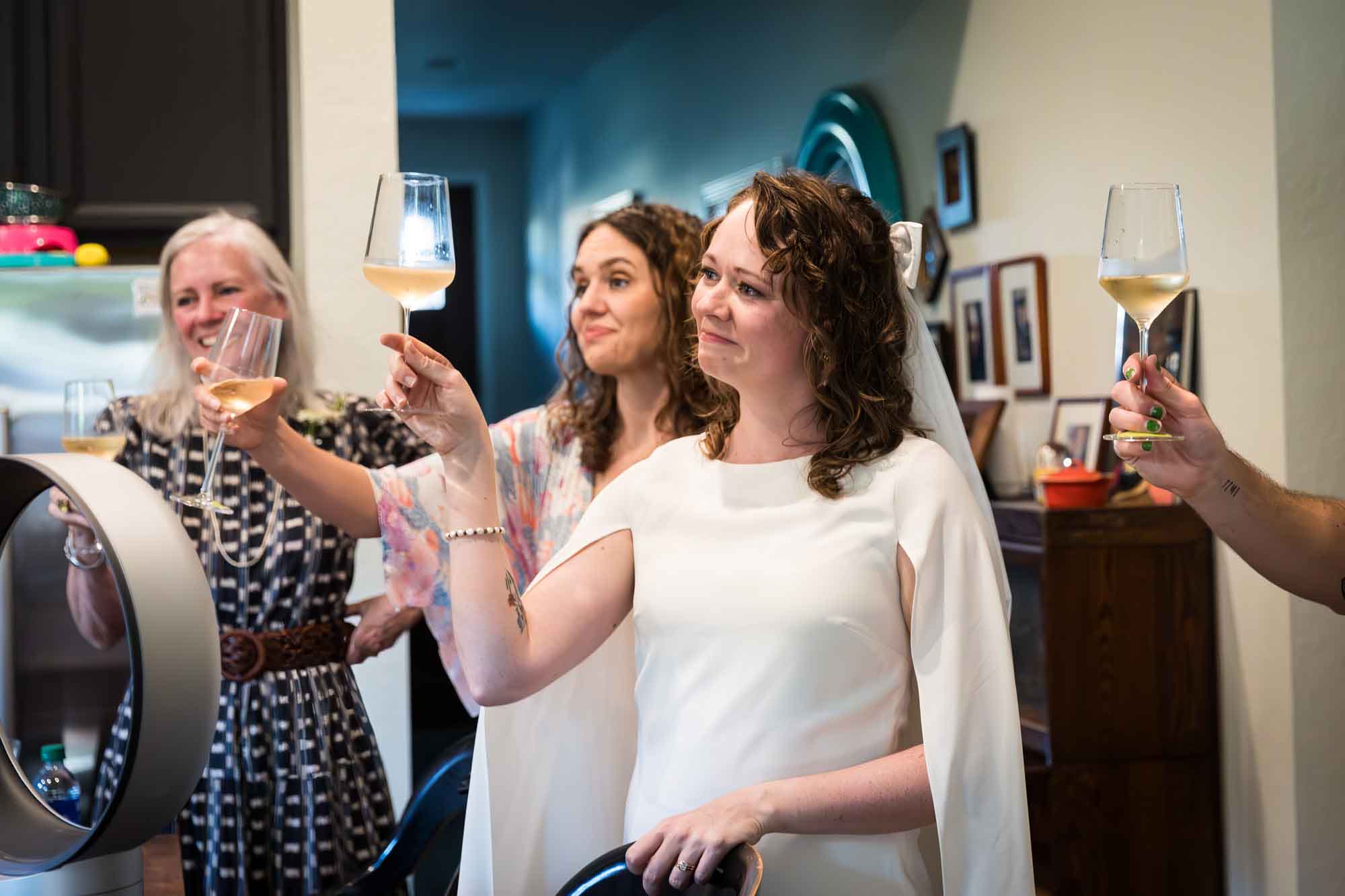 Bride and guests holding up glasses of wine in a kitchen for an article on affordable wedding venues in San Antonio