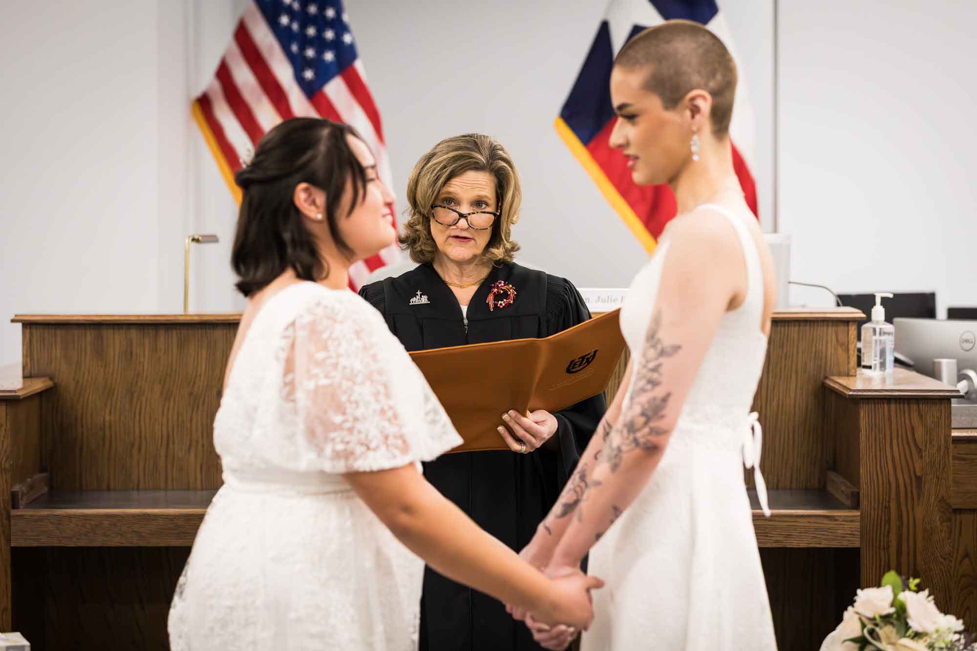 Two brides holding hands and saying vows in front of a judge for an article on affordable wedding venues in San Antonio