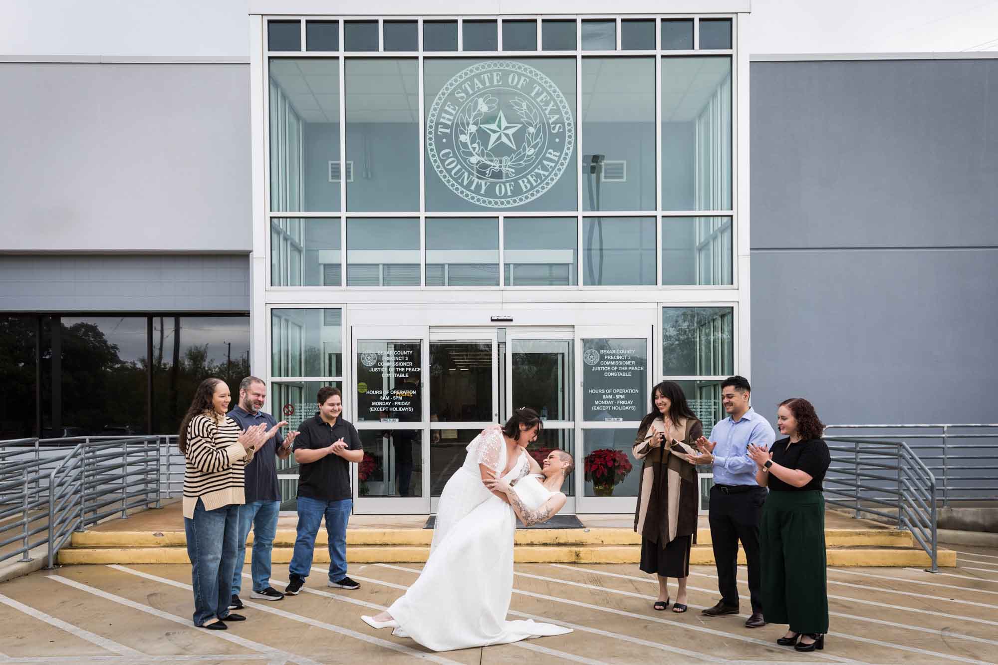 Two brides kissing in a dramatic dip in front of a county courthouse for an article on affordable wedding venues in San Antonio
