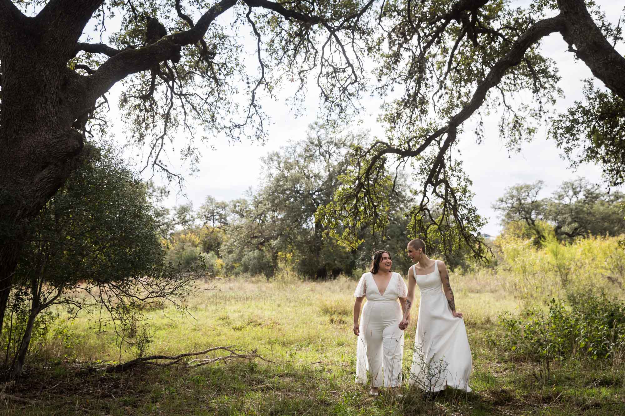 Two brides walking underneath tree branches in a meadow at Walker Ranch Park