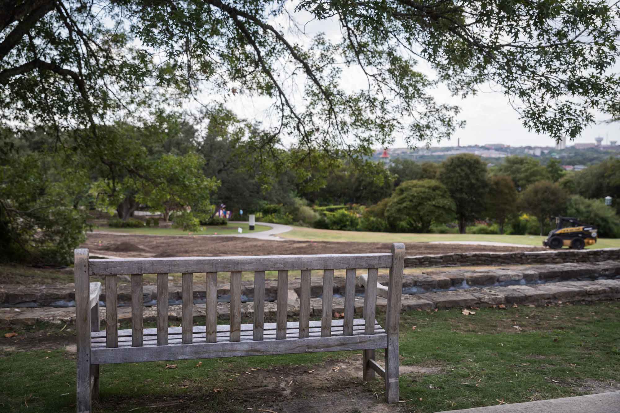Wooden bench at overlooking looking over San Antonio skyline with orange and black construction vehicle moving dirt for an article on the best San Antonio Botanical Garden photo locations