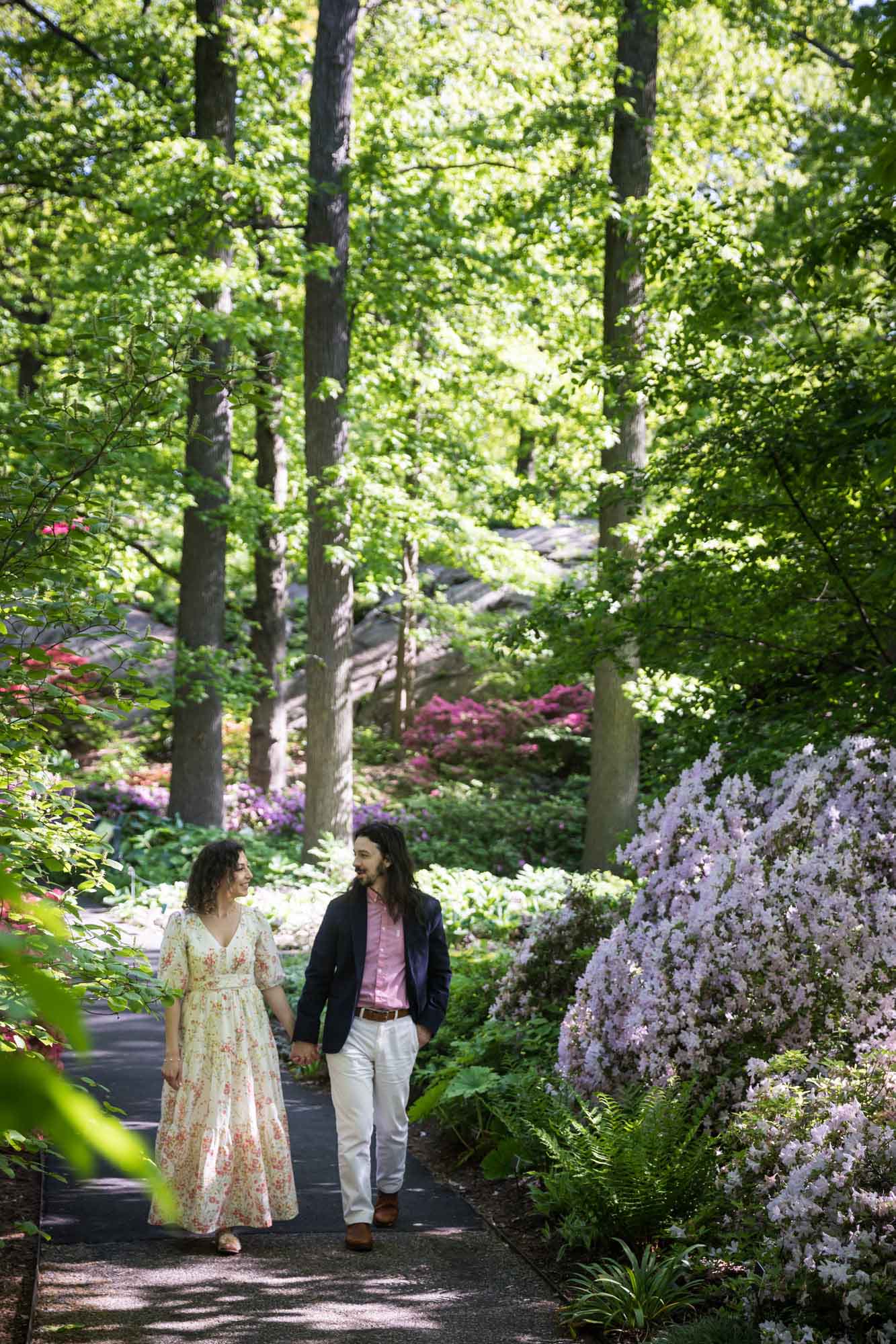 Couple holding hands walking up pathway through forest and azalea bushes for an article on the best San Antonio Botanical Garden photo locations