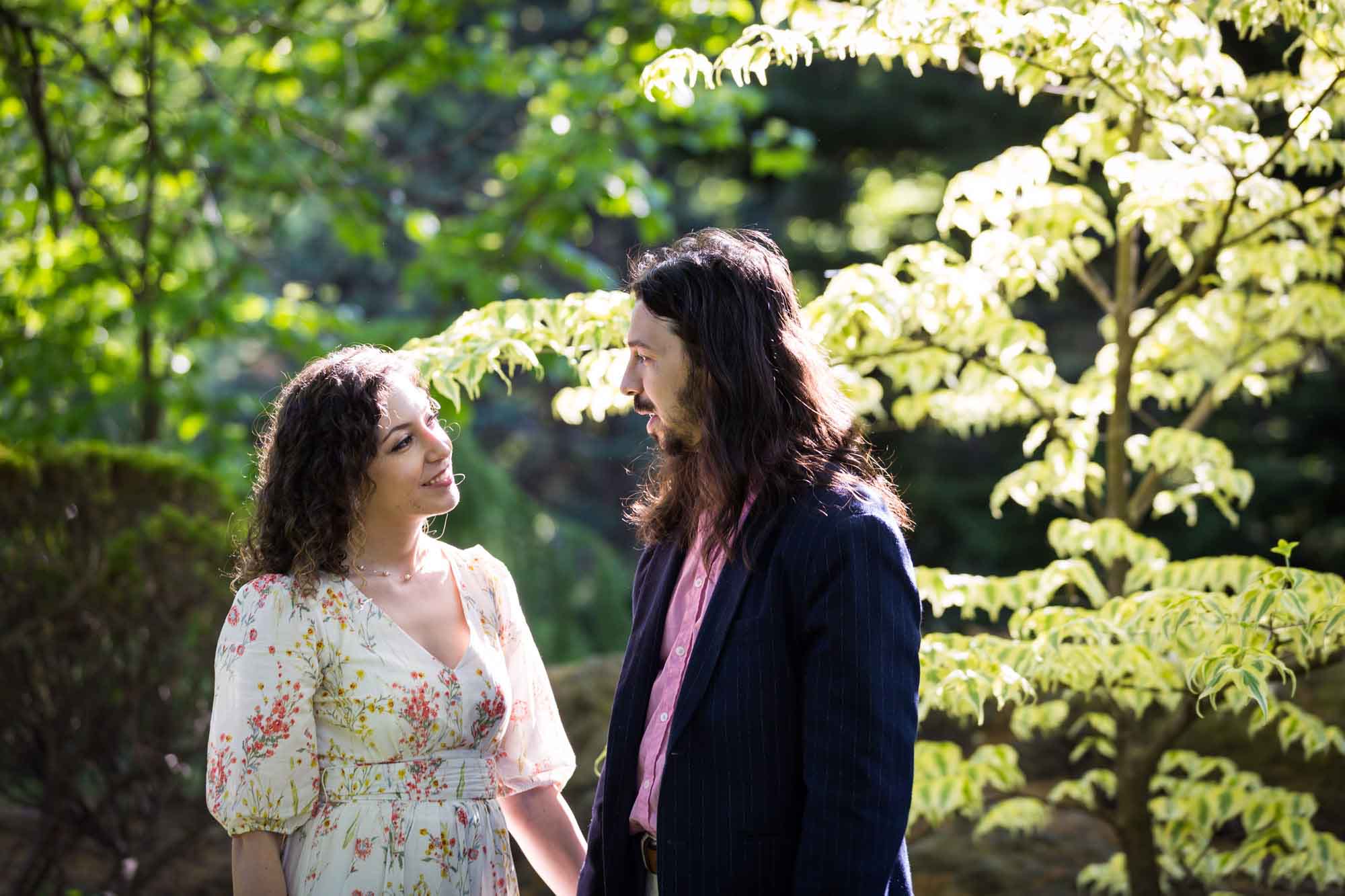 Couple looking at each other in front of trees in sunlight for an article on the best San Antonio Botanical Garden photo locations
