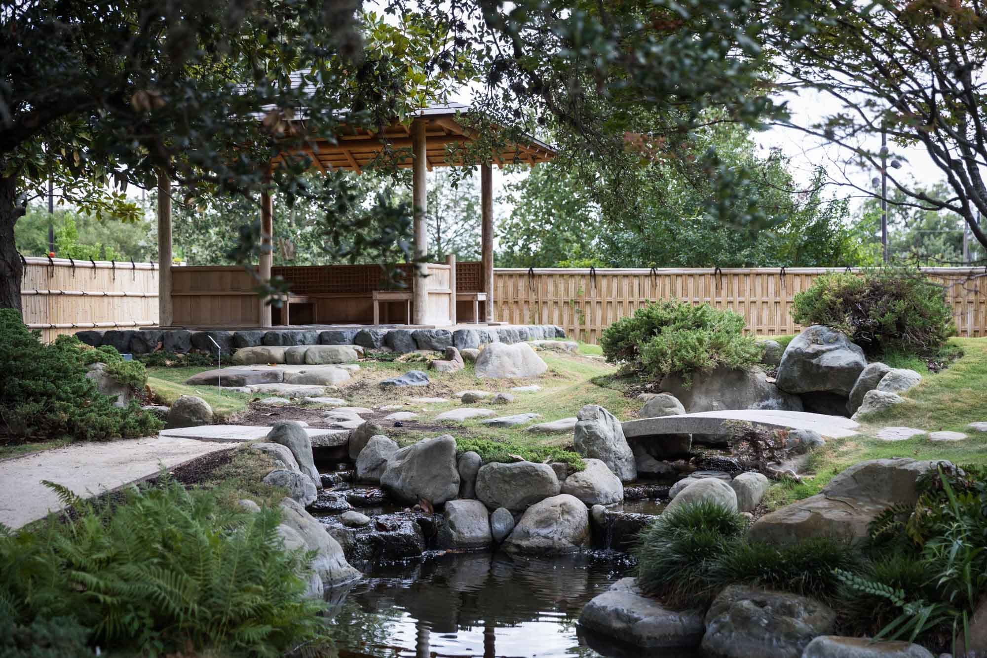 Wide view of Kumamoto En Japanese Garden showing azumaya, pond, bridge, stones, and trees for an article on the best San Antonio Botanical Garden photo locations
