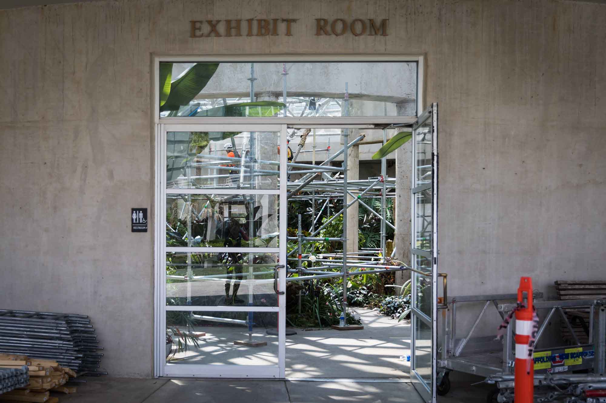 Entrance to the Exhibit Room showing scaffolding inside, glass door open, and construction materials outside the entrance for an article on the best San Antonio Botanical Garden photo locations