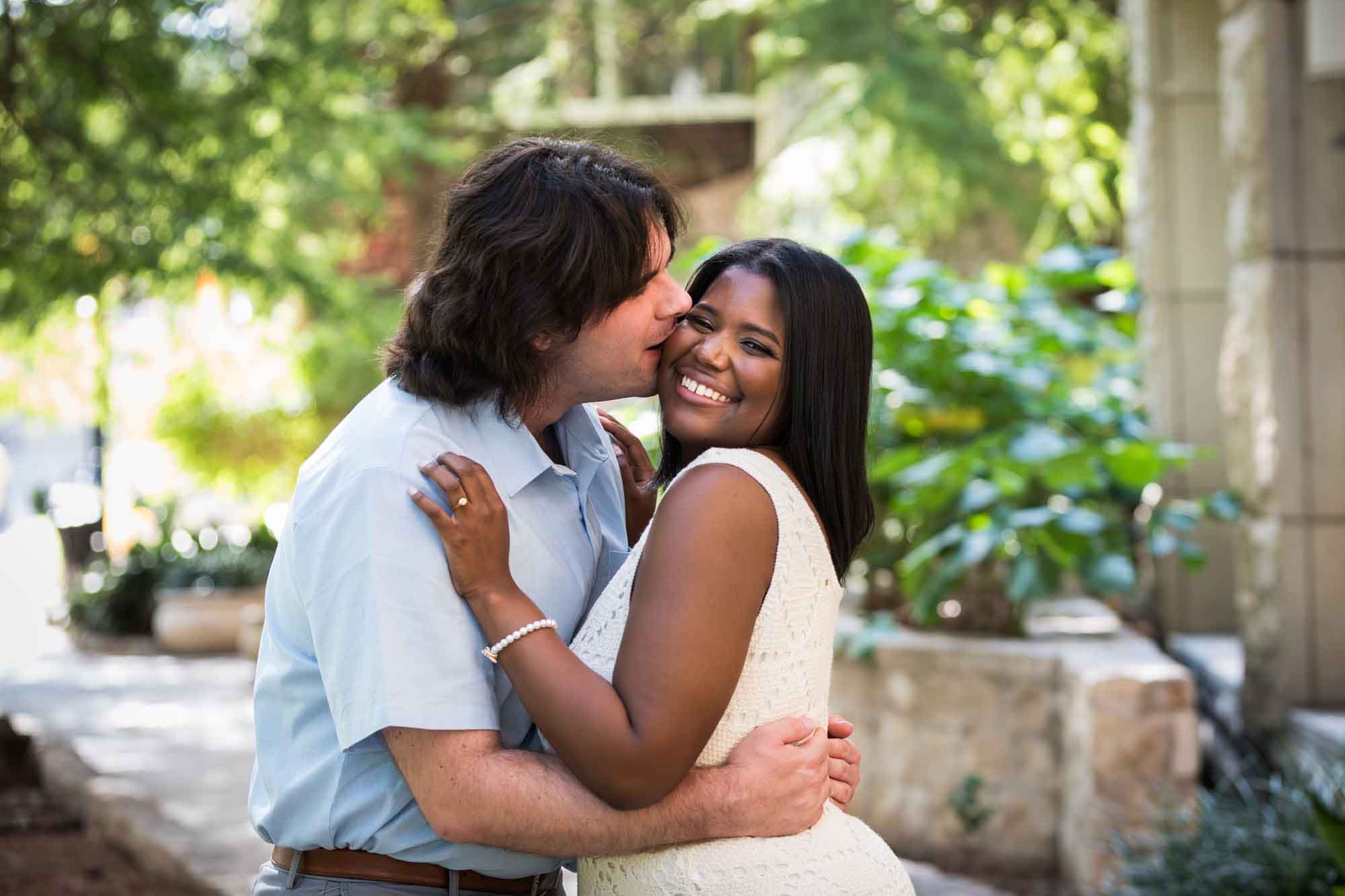 African American woman wearing white sleeveless dress being kissed by fiance wearing blue shirt for an article on how to get married on a River Walk boat