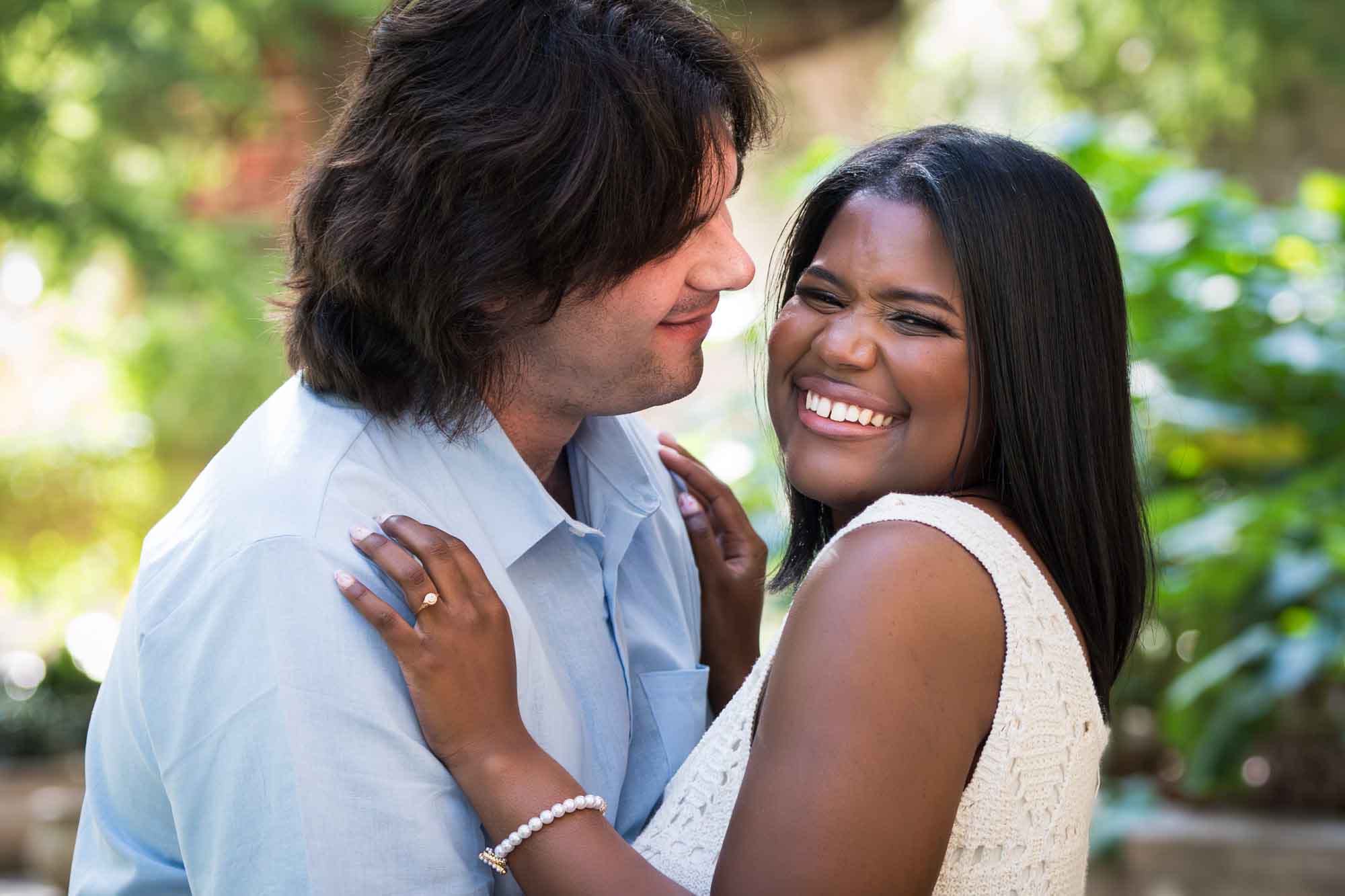 African American woman wearing white sleeveless dress hugging fiance wearing blue shirt African American woman wearing white dress dancing with white fiance on River Walk pathway beside river for an article on how to get married on a River Walk boat