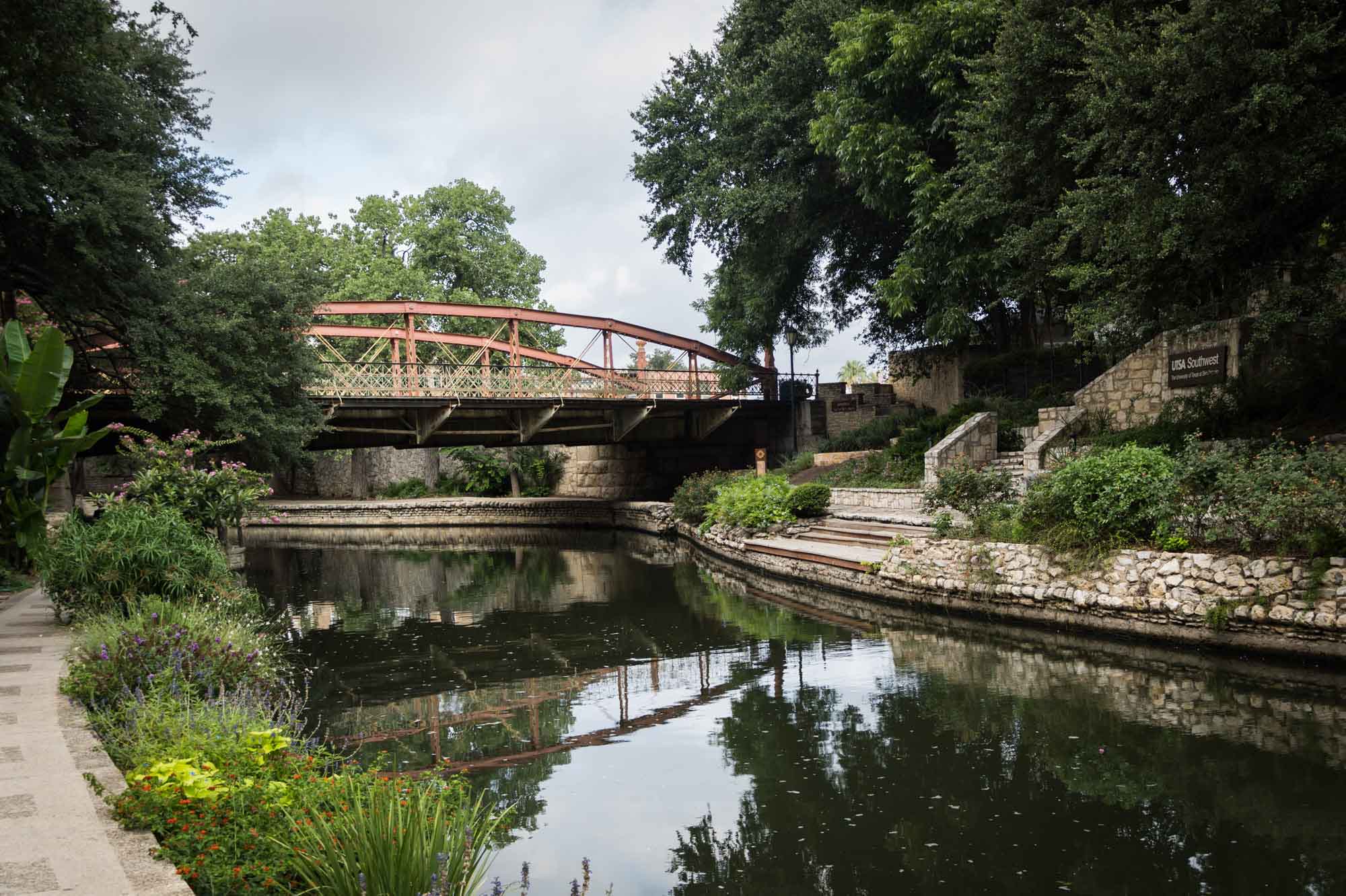 Scene along the River Walk in San Antonio, Texas with red bridge, stone walls, and landscaping