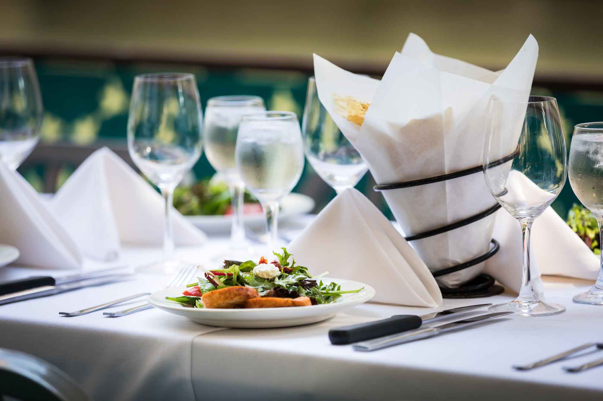 Table set with white tablecloth, glasses, and plate with salad for an article on how to get married on a River Walk boat