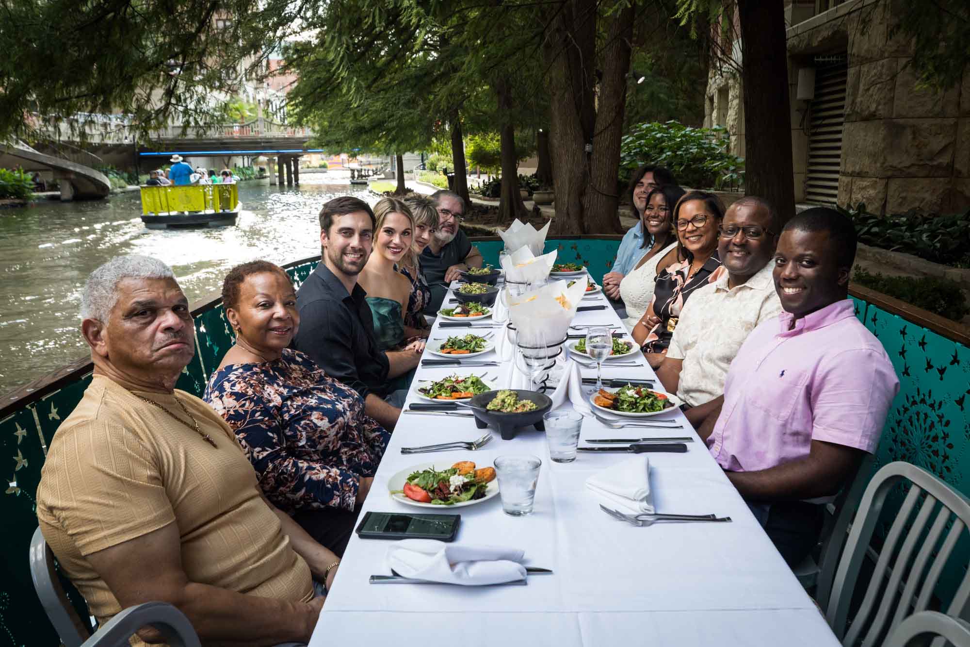 Posed portrait of guests seated at long table with white tablecloth and plates with salads on boat for an article on how to get married on a River Walk boat