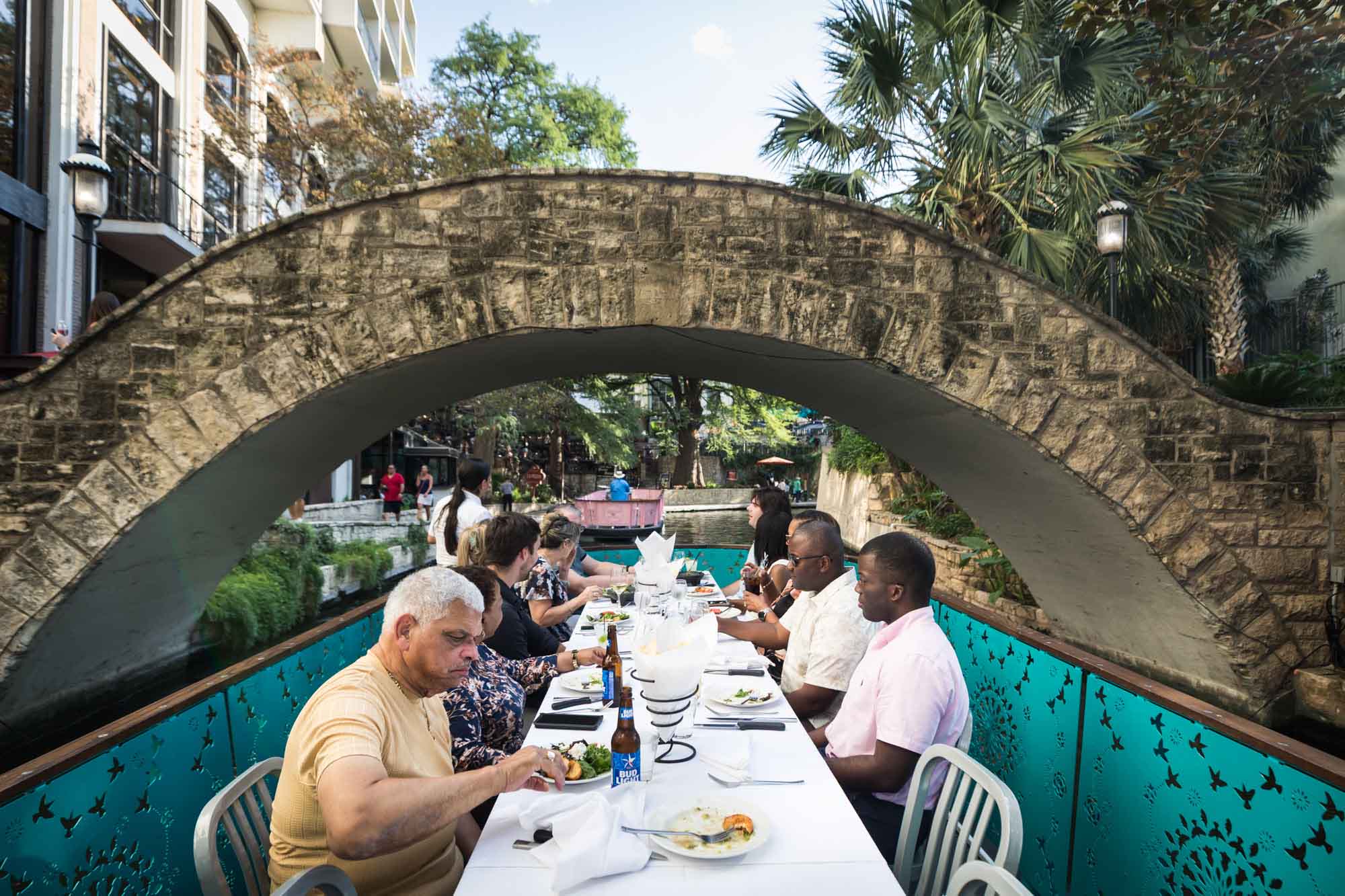 Guests seated at table on River Walk boat floating under stone bridge for an article on how to get married on a River Walk boat
