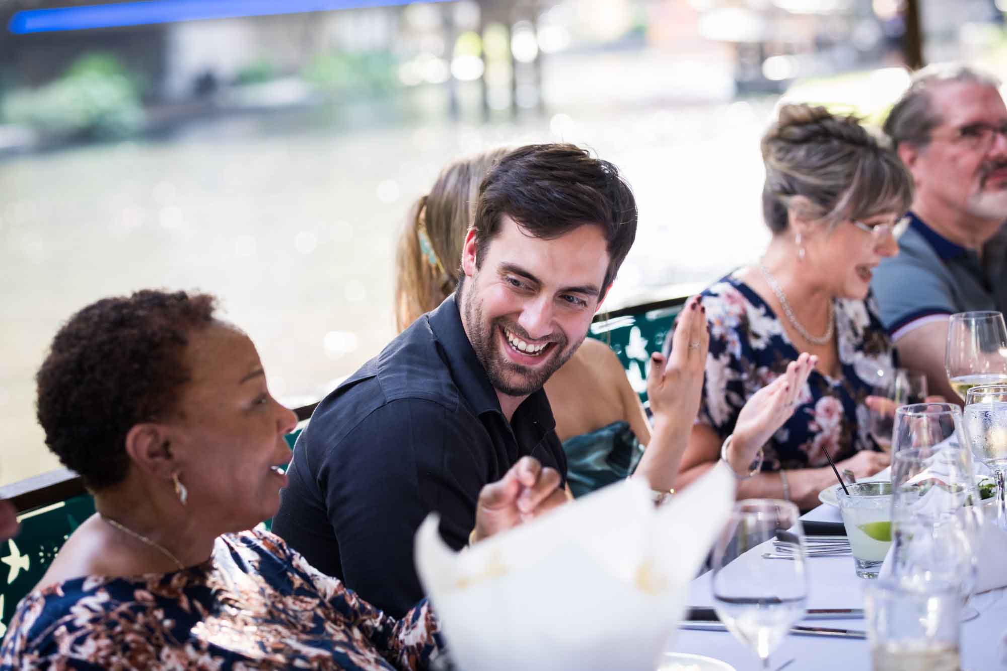 Man smiling with goatee surrounded by woman seated at table for an article on how to get married on a River Walk boat