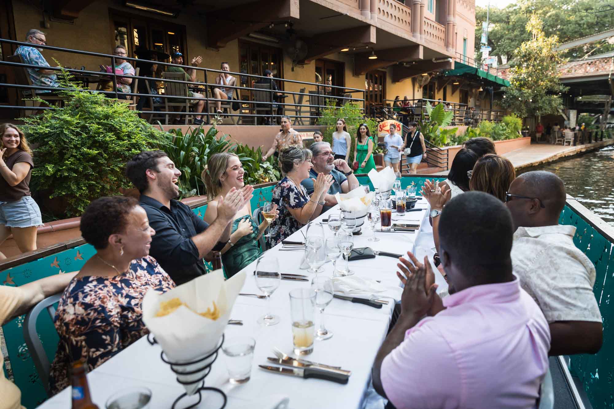 Table surrounded by guests clapping on River Walk boat beside restaurant for an article on how to get married on a River Walk boat